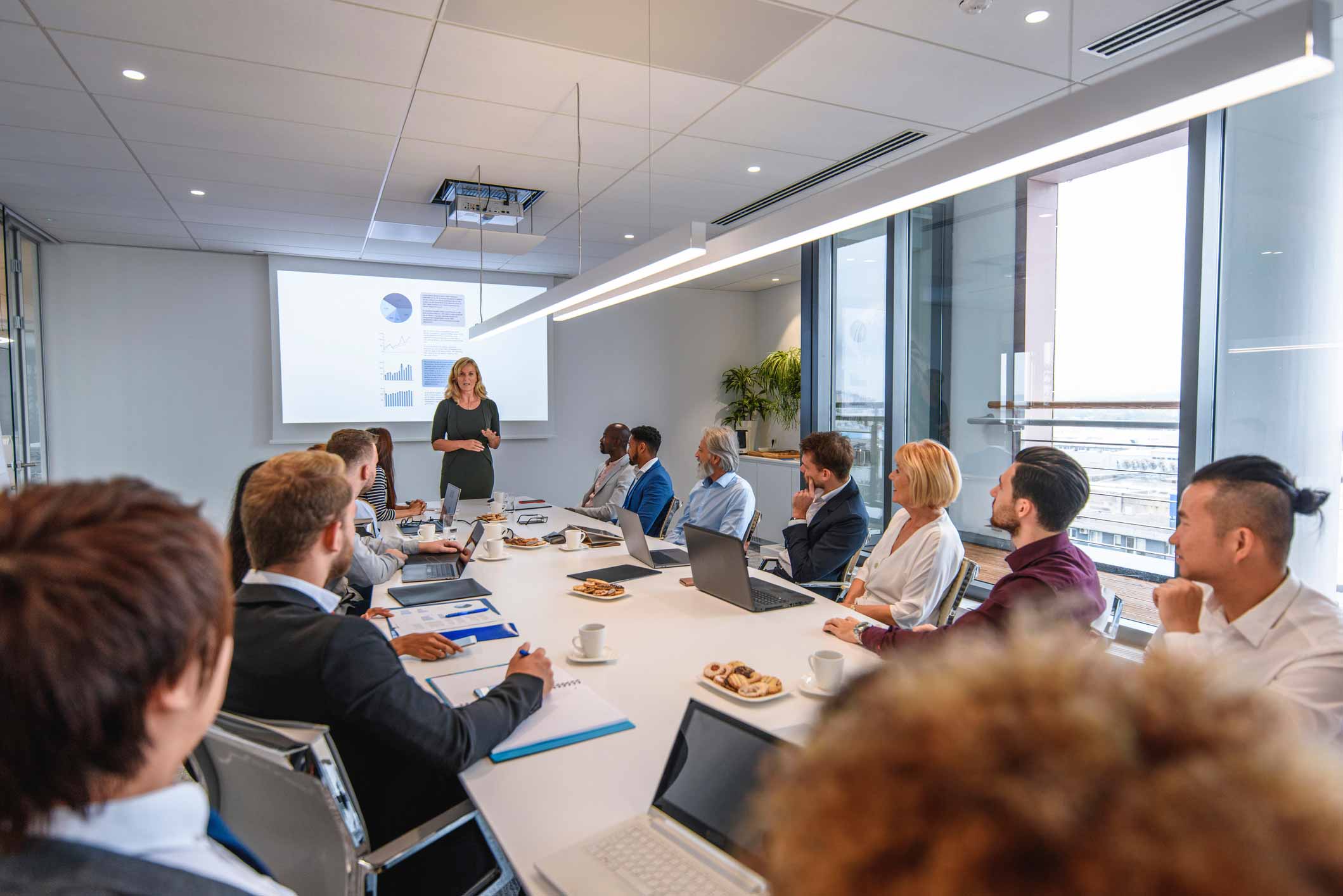 People in a conference room watch a woman present on mobile device management consulting services.