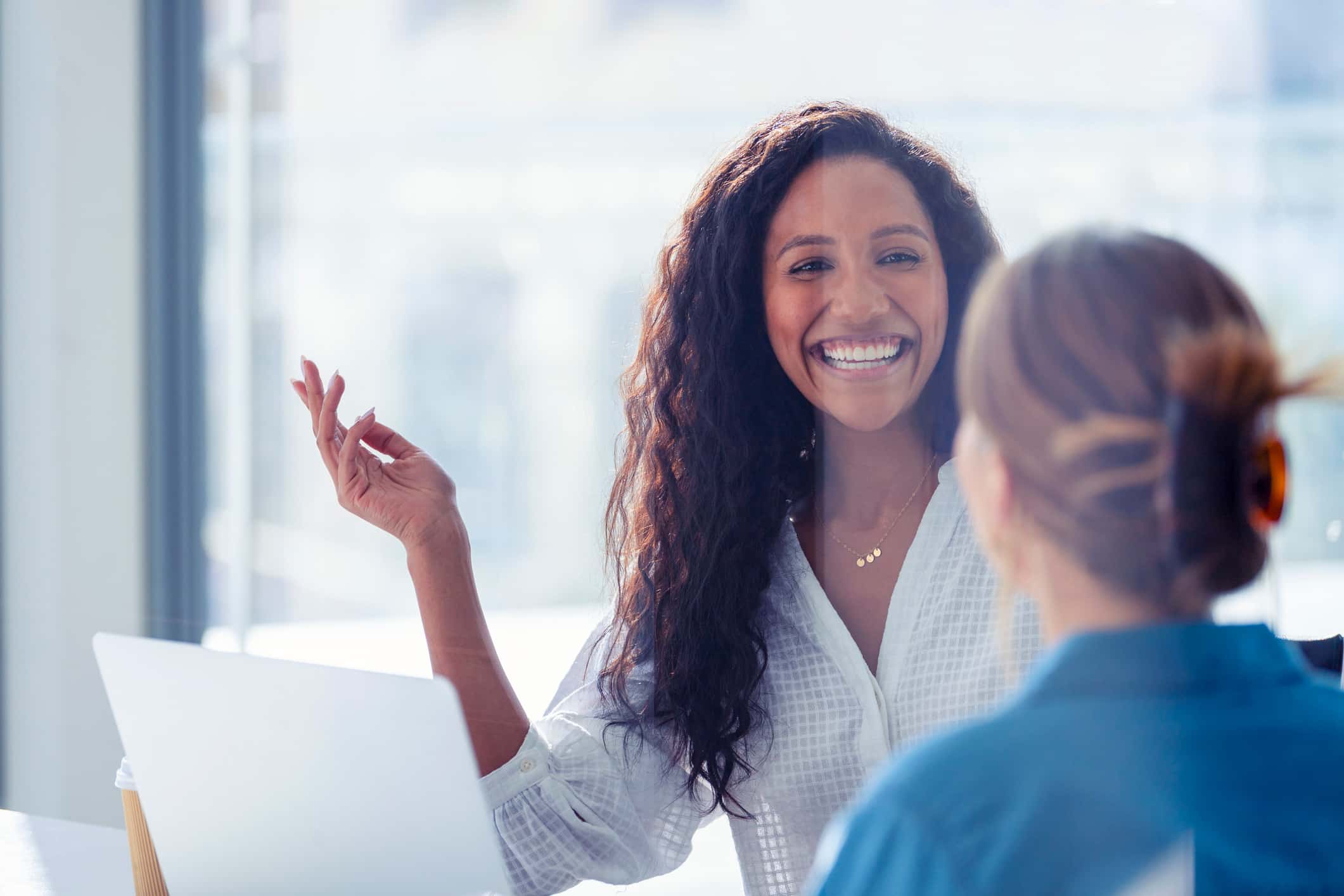 Smiling woman discussing Client Relationship Management with a colleague in an office setting.