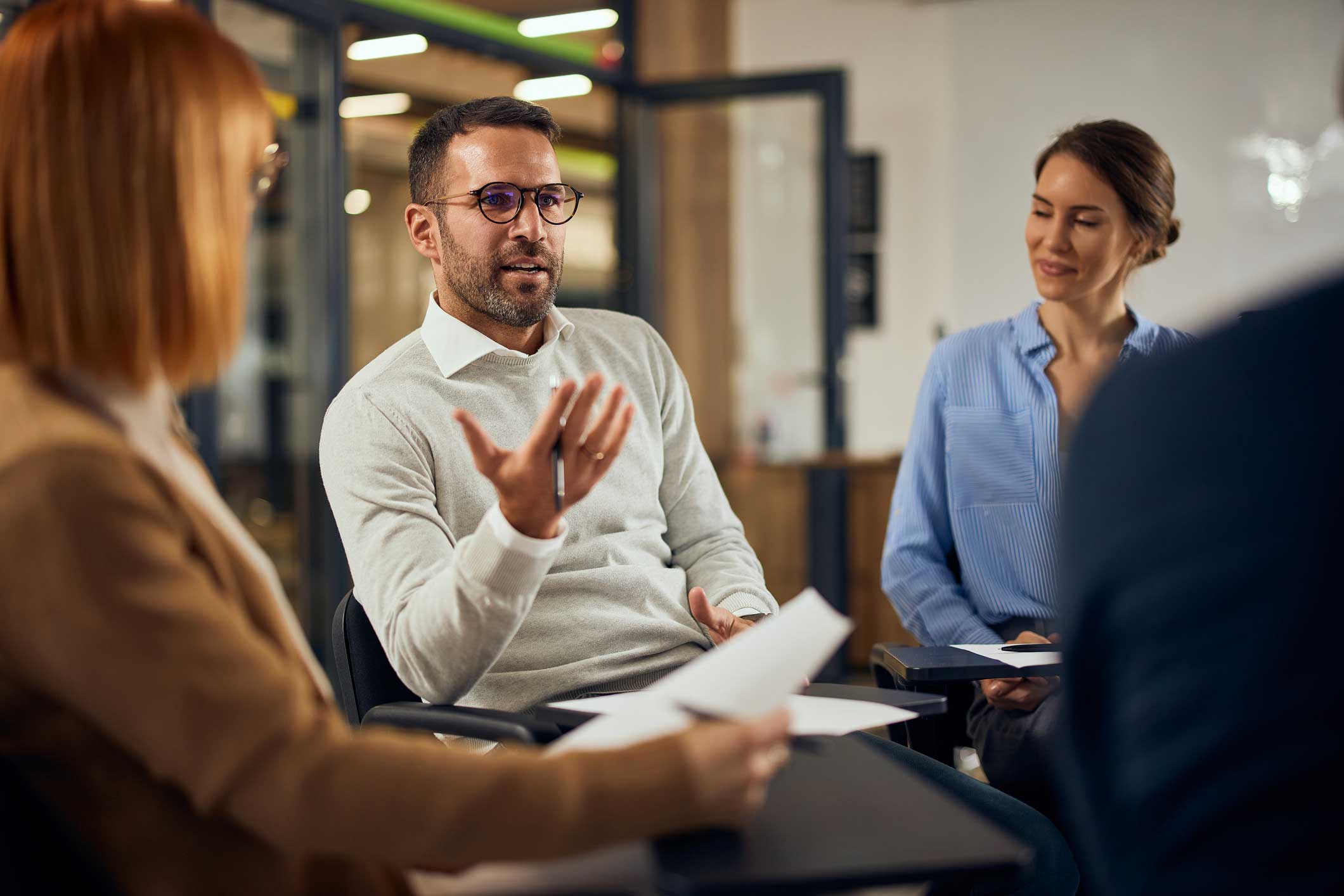 Man discussing Digital Forensics Reporting in a group meeting, as two women listen and take notes.
