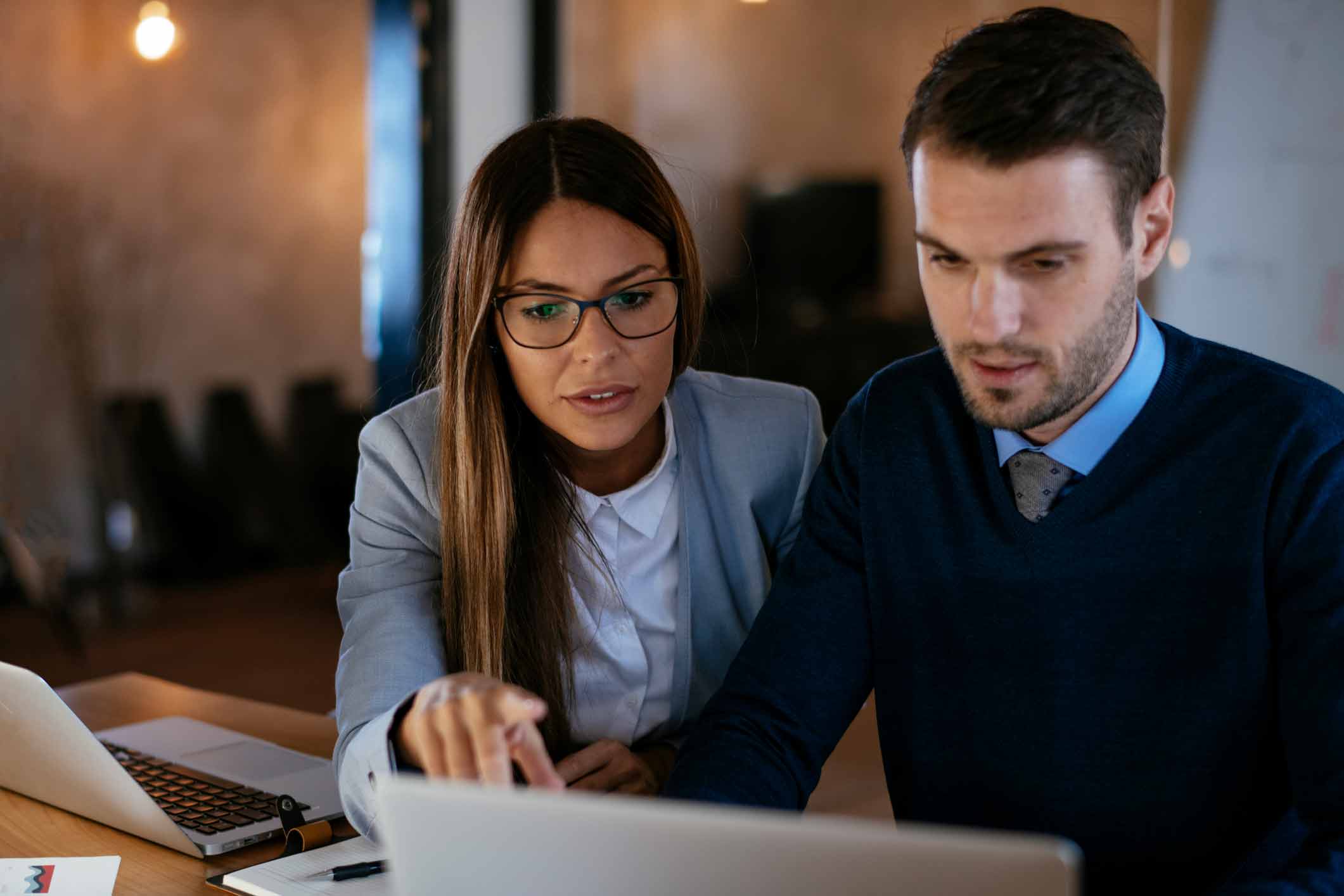 Two colleagues discuss work and data breach consulting services over a laptop in the office.