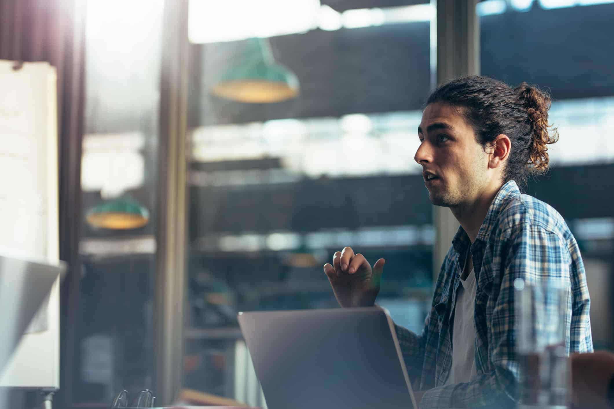 Man with long hair in plaid shirt works on laptop, reviewing Expense Reduction Consulting Services.