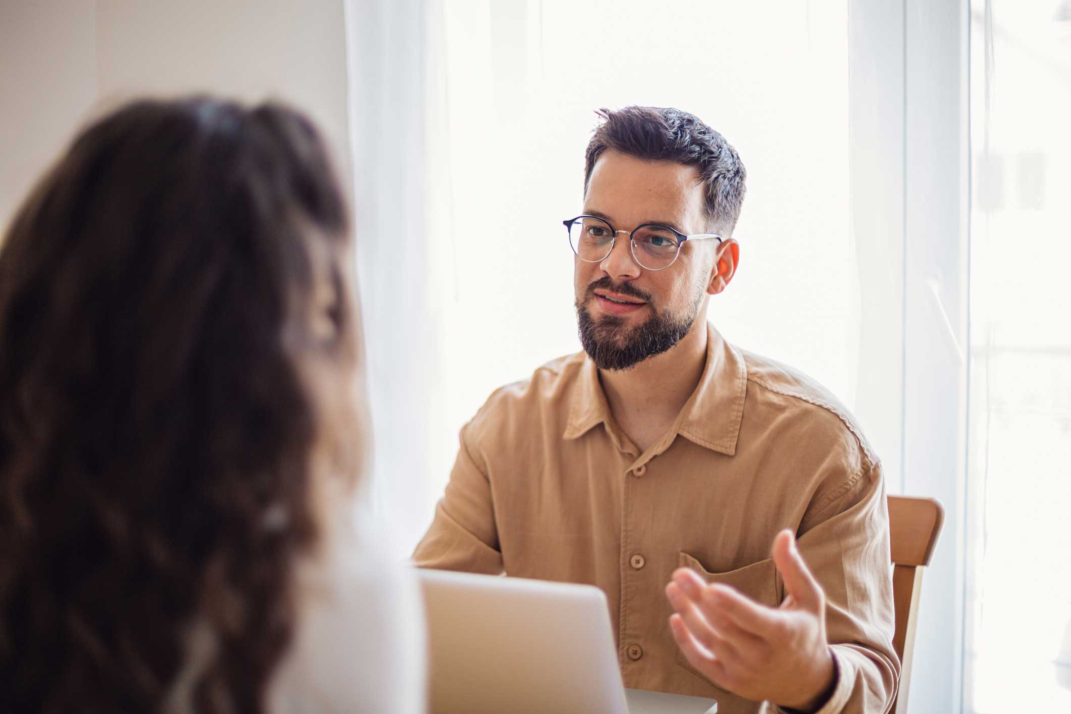 Man with glasses from a cybersecurity compliance consulting firm talks to woman at table.
