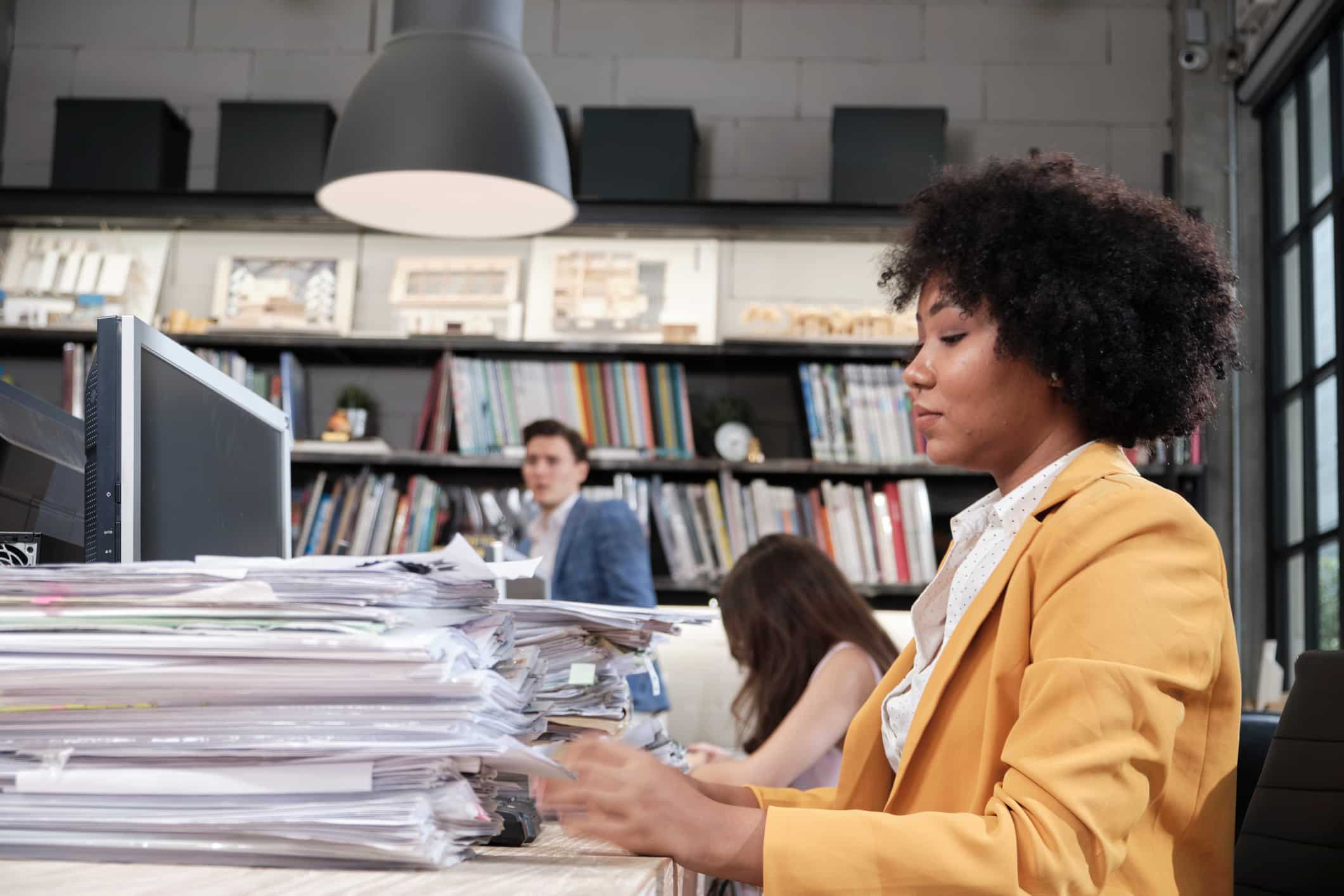 Woman in yellow blazer reviews stacks of papers during eDiscovery Document Review Process.
