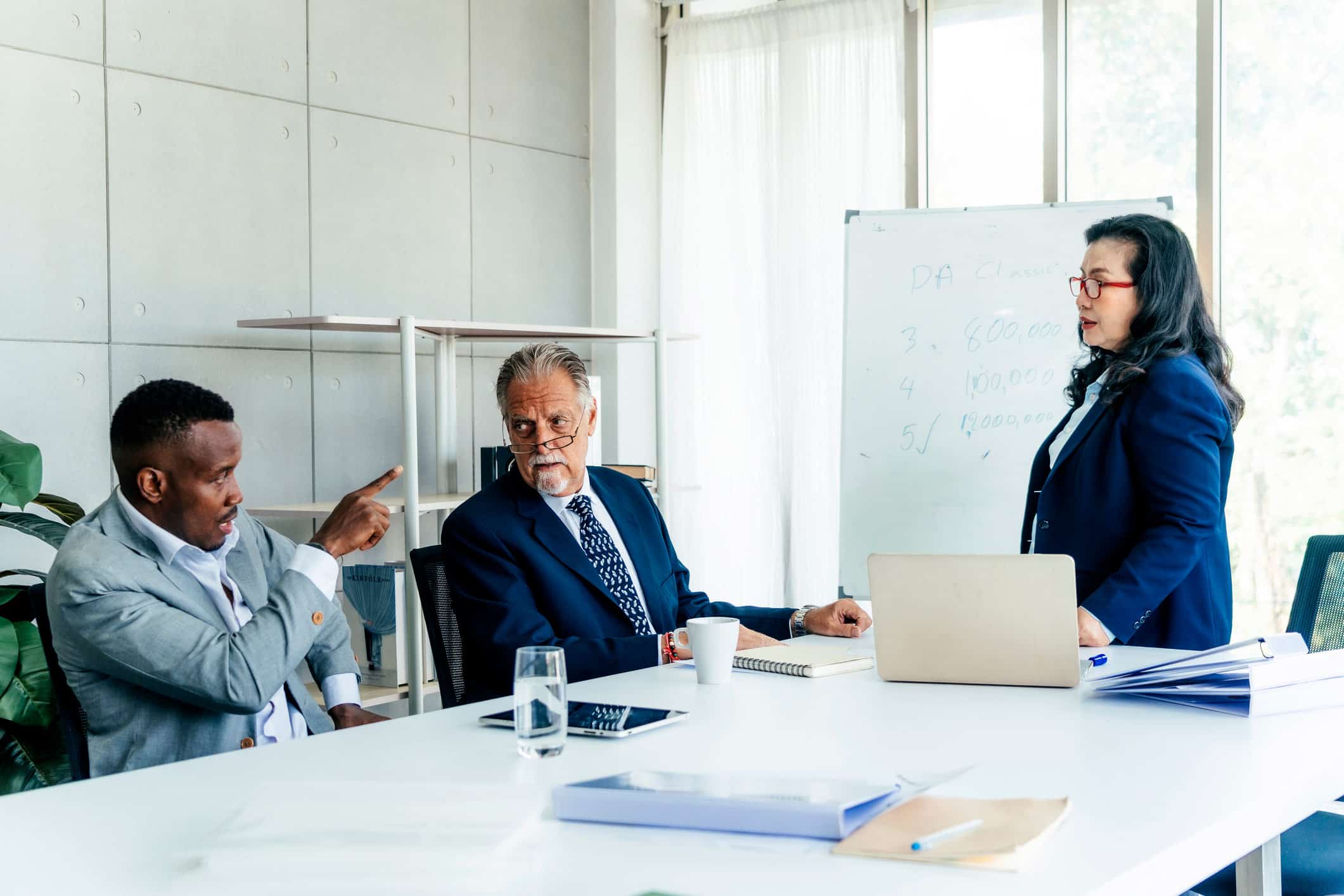 Older man in a suit discusses Forensic Litigation Advisory with colleagues at a conference table.