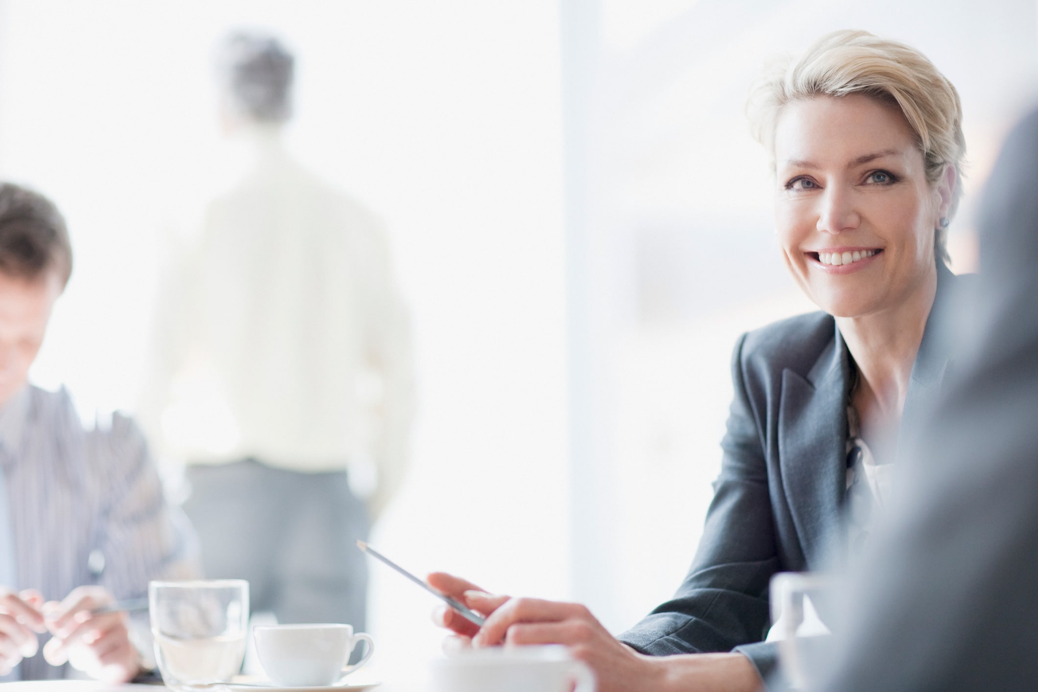 Smiling businesswoman holding a pen at a Review Team Coordination meeting with colleagues.