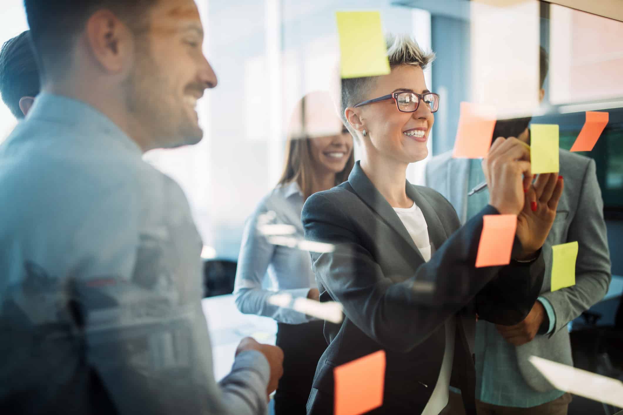 Smiling team members brainstorming TAR Training ideas with colorful sticky notes on a glass wall.
