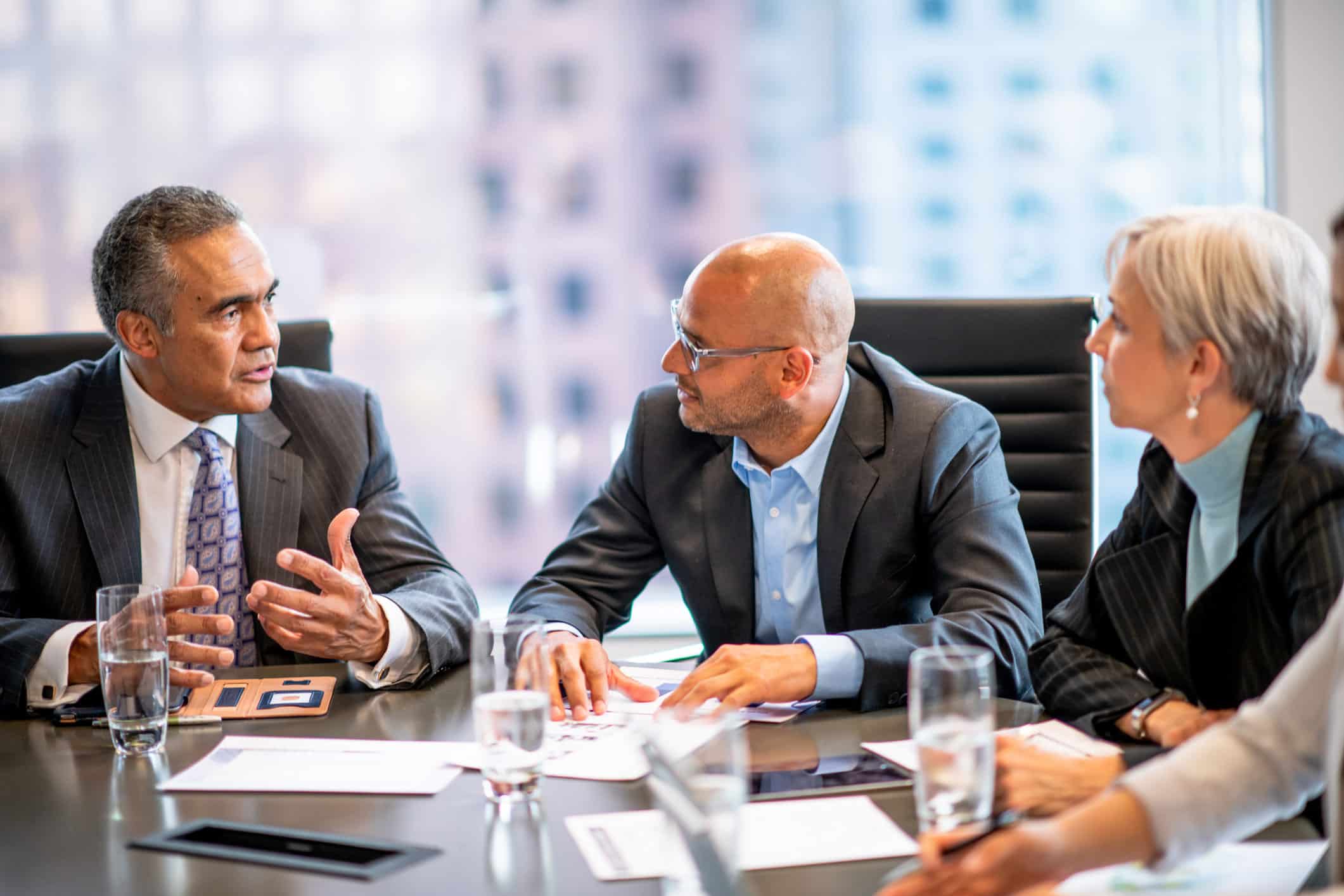 Three businesspeople discuss compensation strategy in a modern consulting firm office.