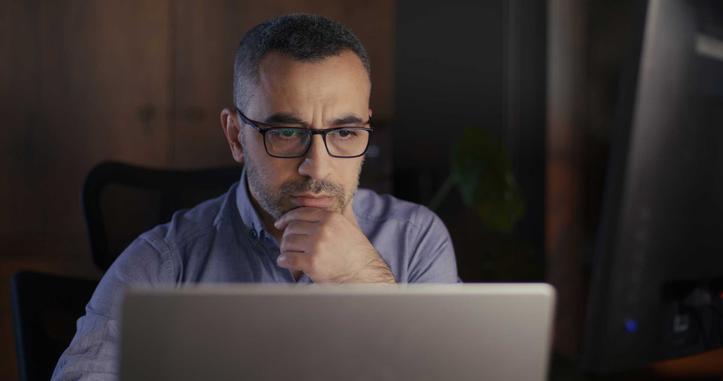 A man wearing glasses thoughtfully reviews AI Legal Document Analysis Consulting on his laptop.