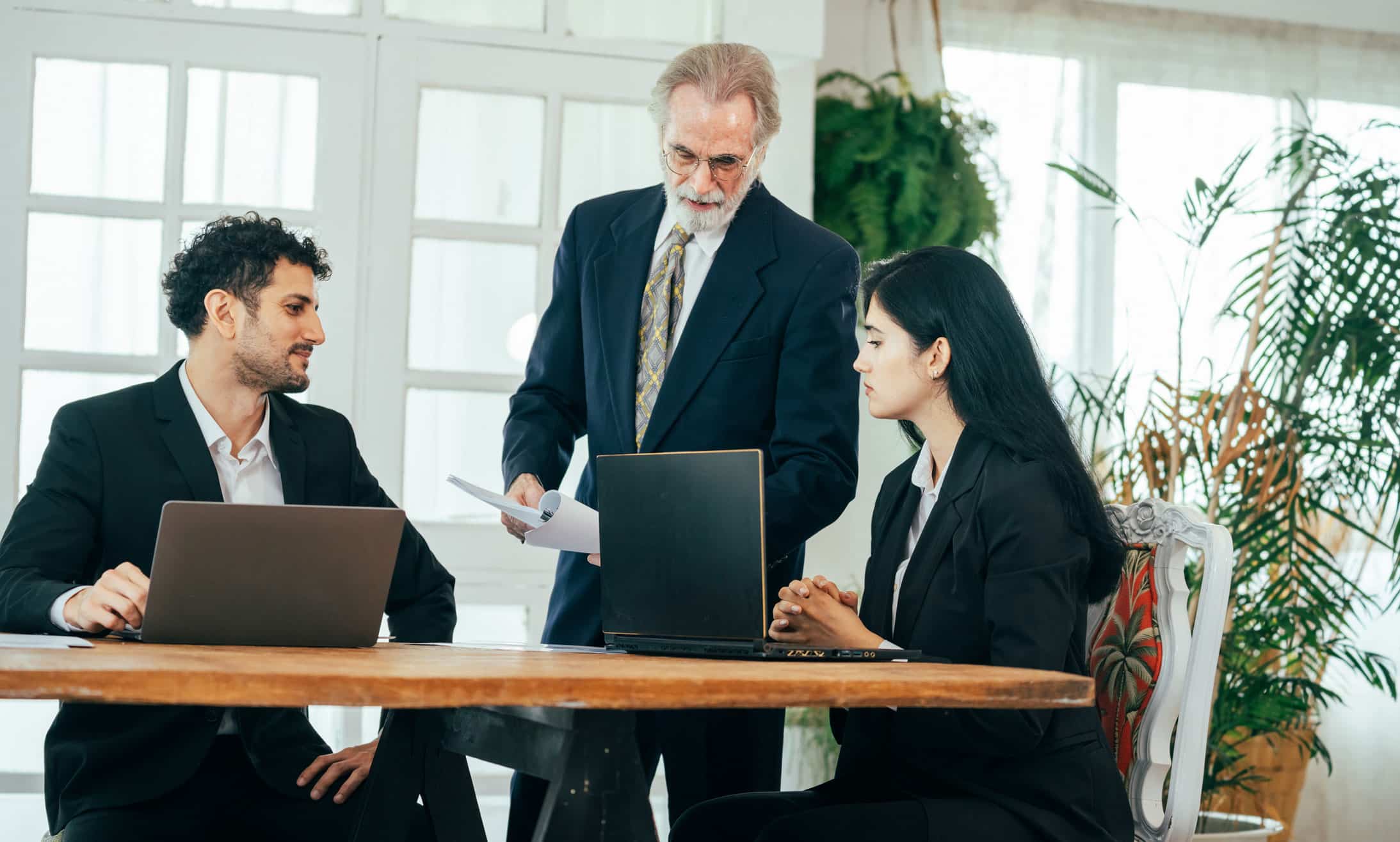 Three businesspeople discuss organizational strategy enablement around a table with laptops.