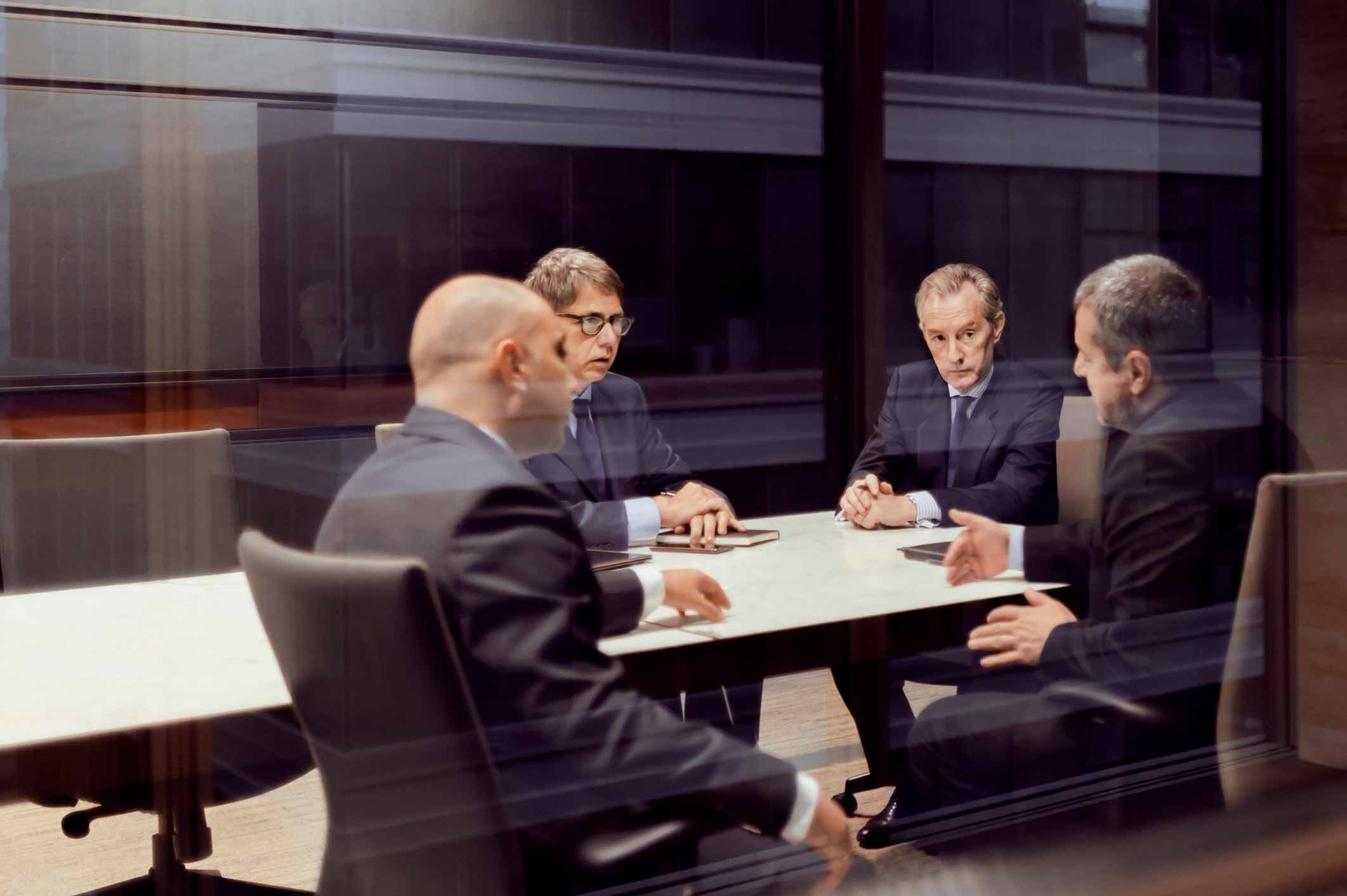 Four men in business suits discuss document management consulting services at a conference table.