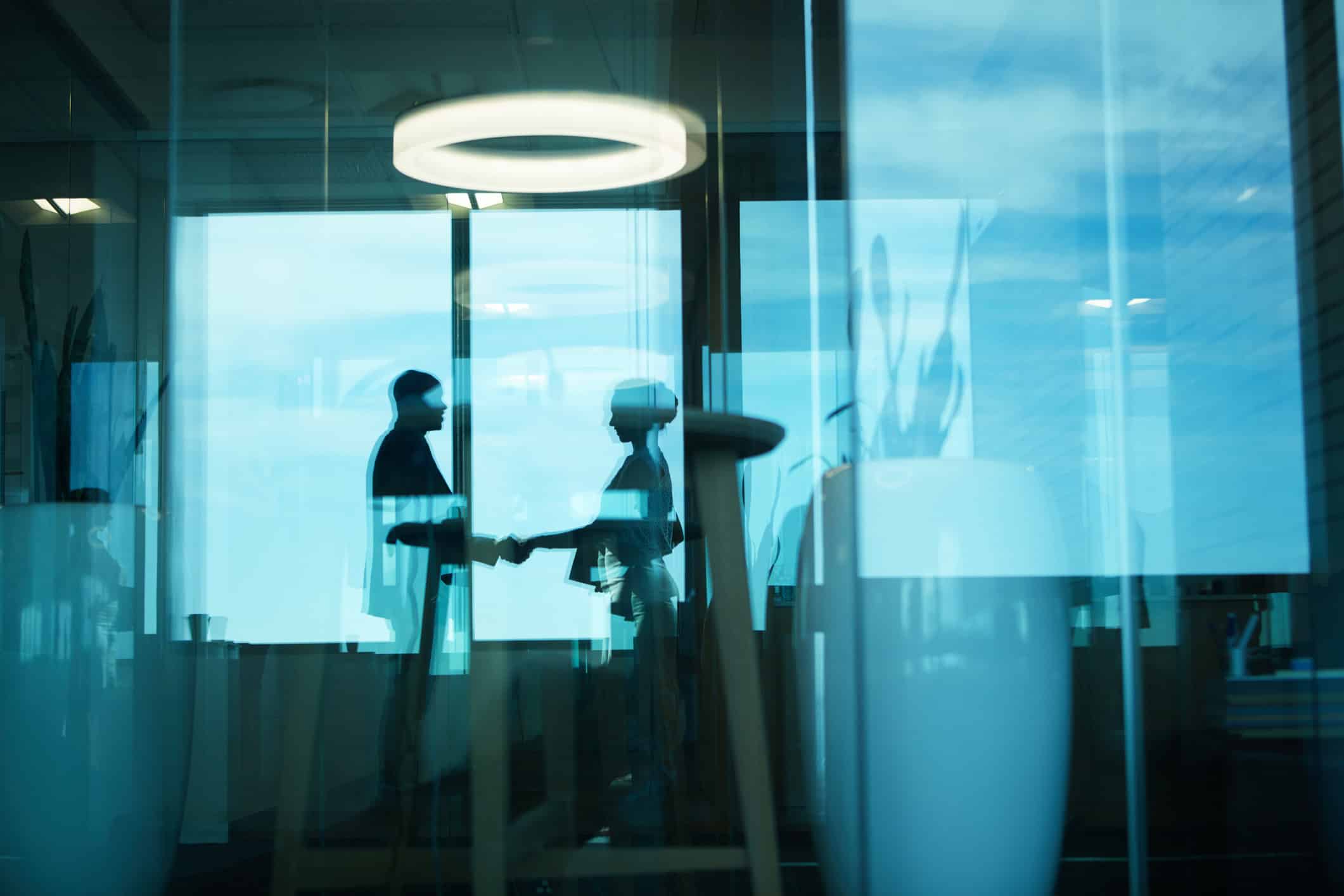 Two people shake hands in an office, reflecting blue and Expense Reduction Optimization.