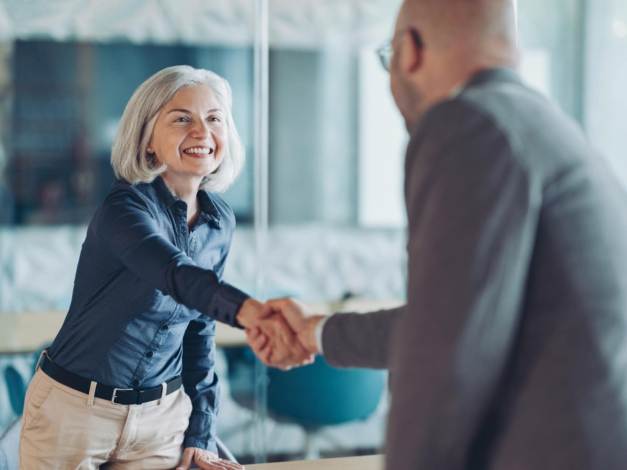 Smiling woman with gray hair shakes hands with a man in a law firm marketing development office.