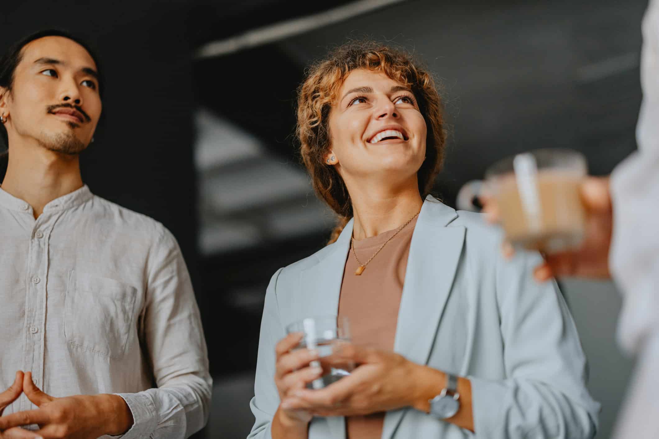 Smiling woman holding a glass, discussing workforce development planning with others indoors.