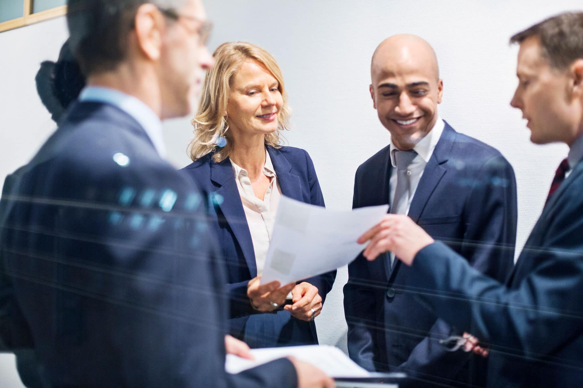Four business professionals in suits discussing Business Valuation documents in an office setting.