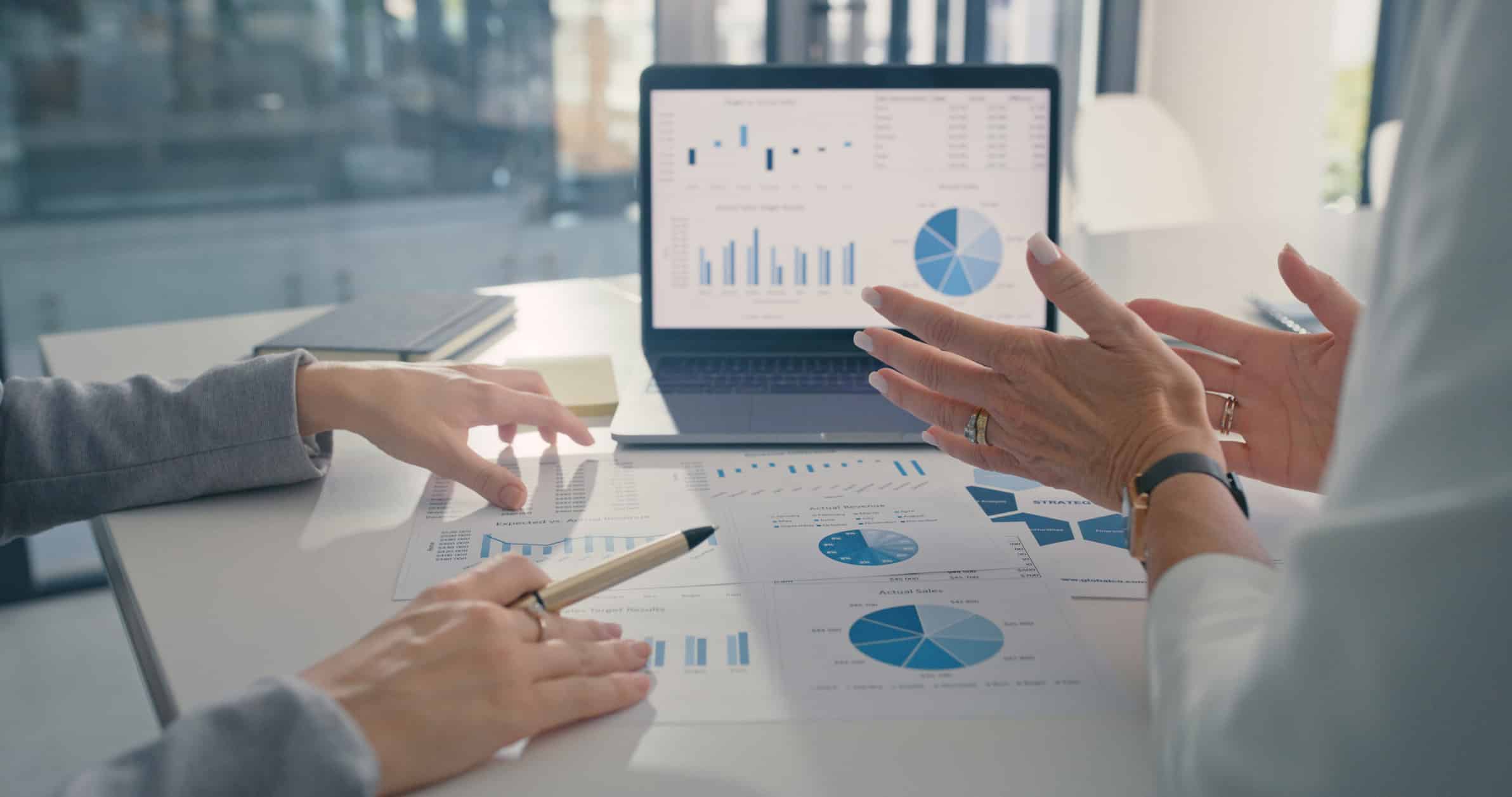 Two people discuss Expense Reduction Structuring with charts and graphs at an office desk.