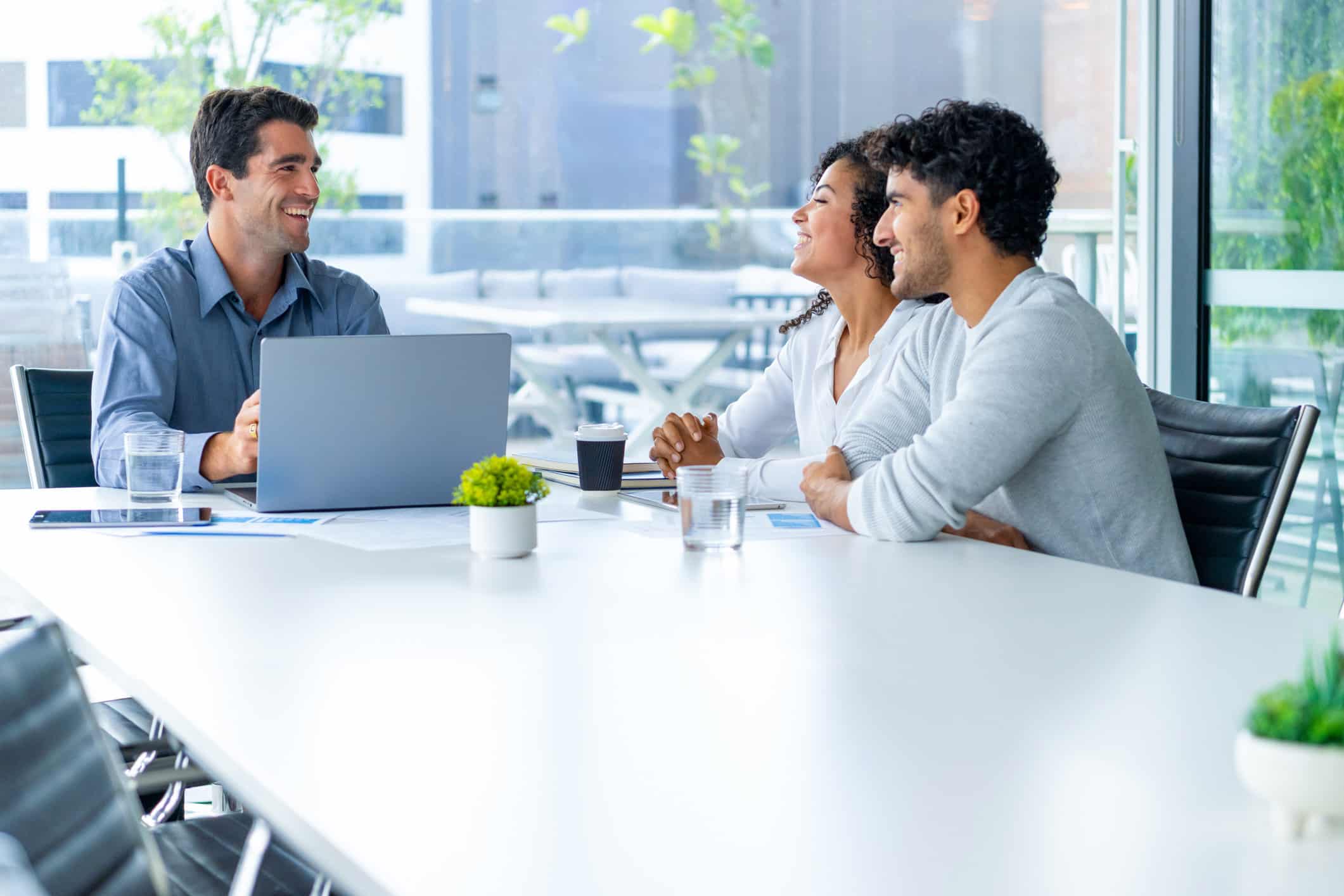 Three people discuss Strategic M&A Deal Framing at a table with a laptop in a bright office.