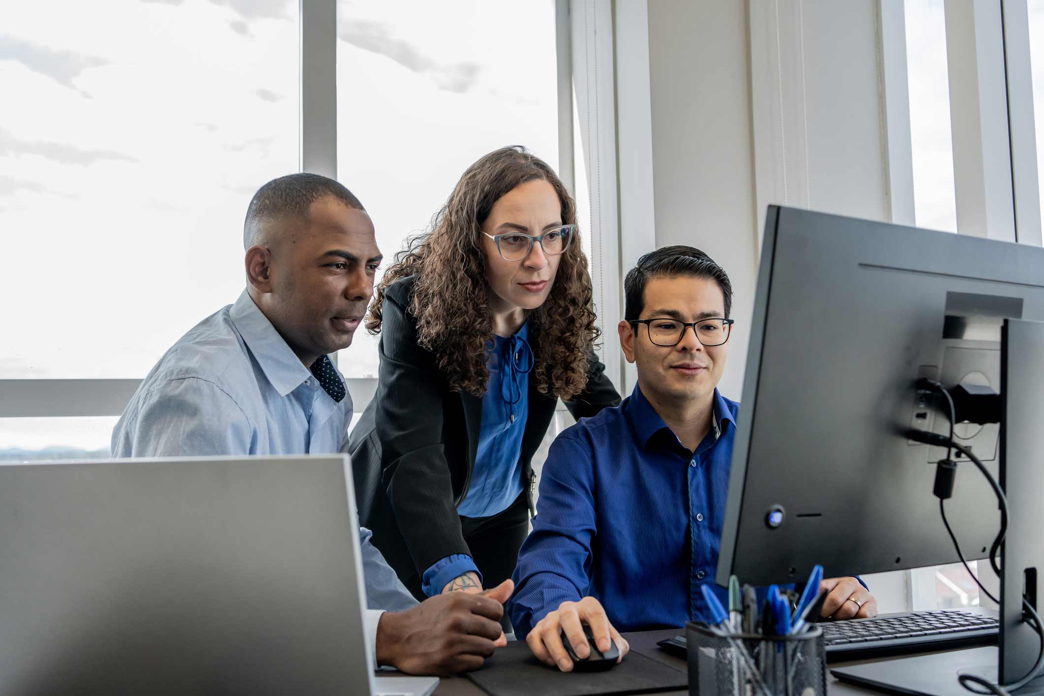 Three colleagues review IAM Strategic Execution on a computer in a modern office setting.