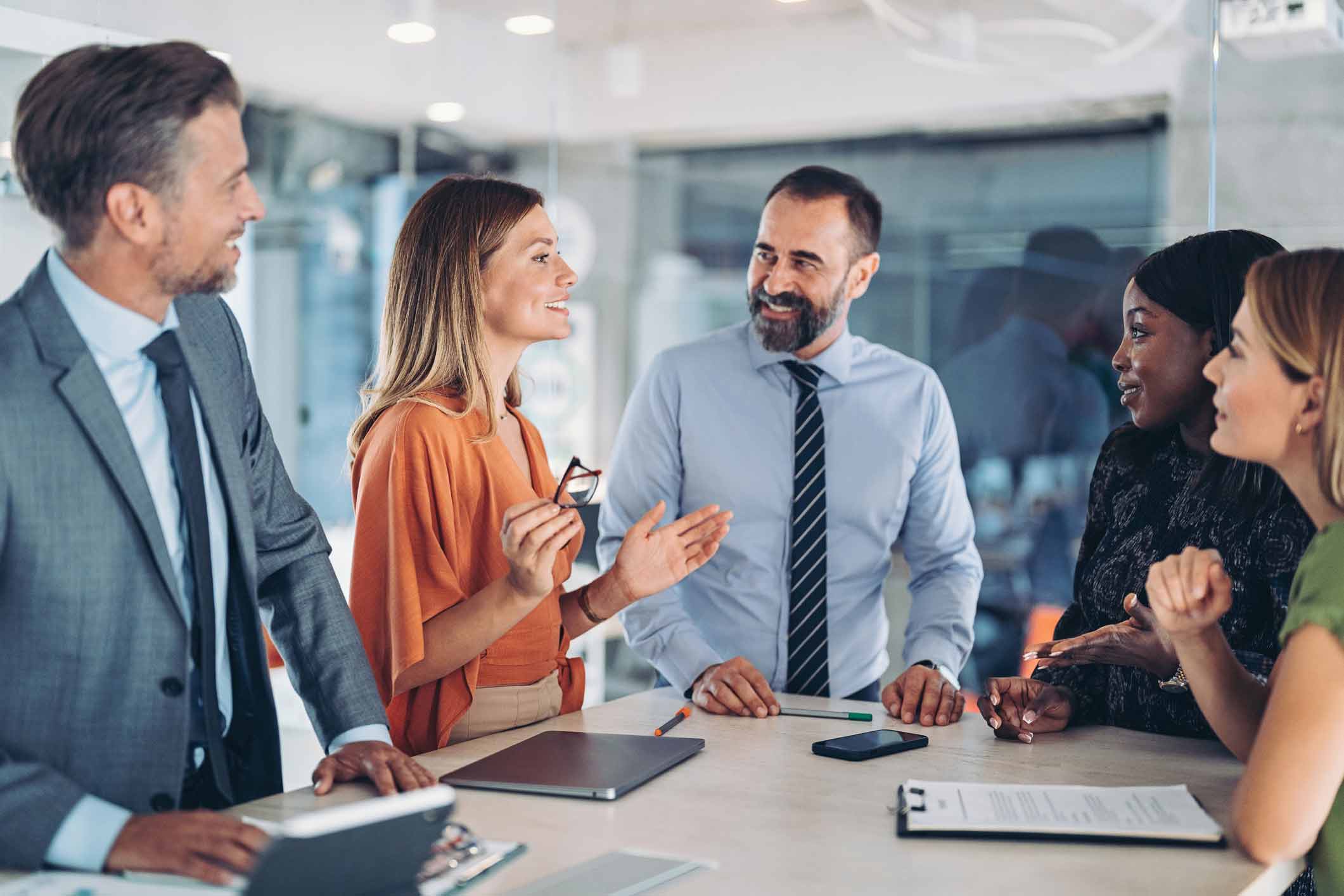Five business people discuss Machine Learning Execution while smiling around a table in an office.