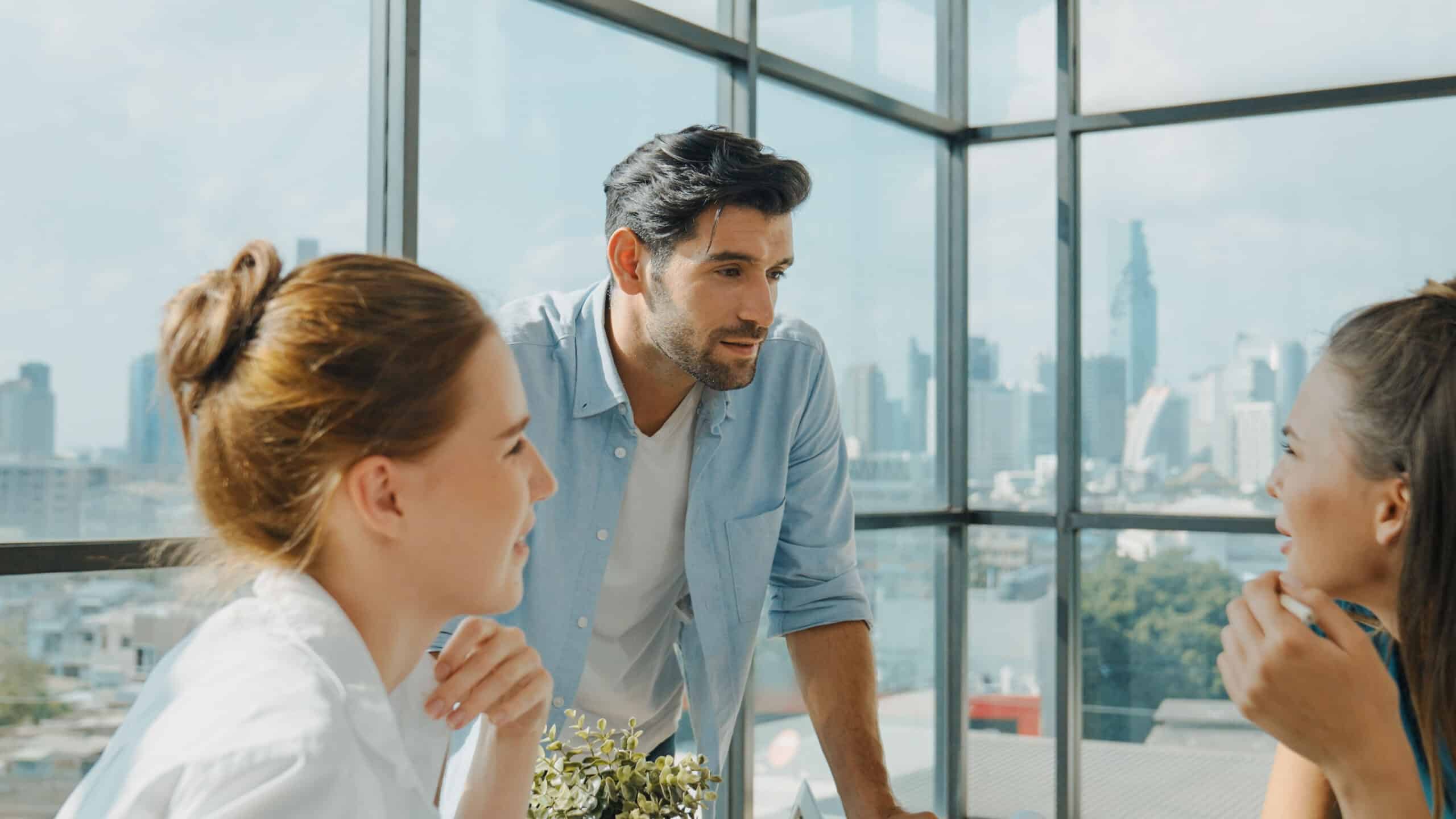 Three people discuss Big Data Strategy Execution in a bright office with city views.