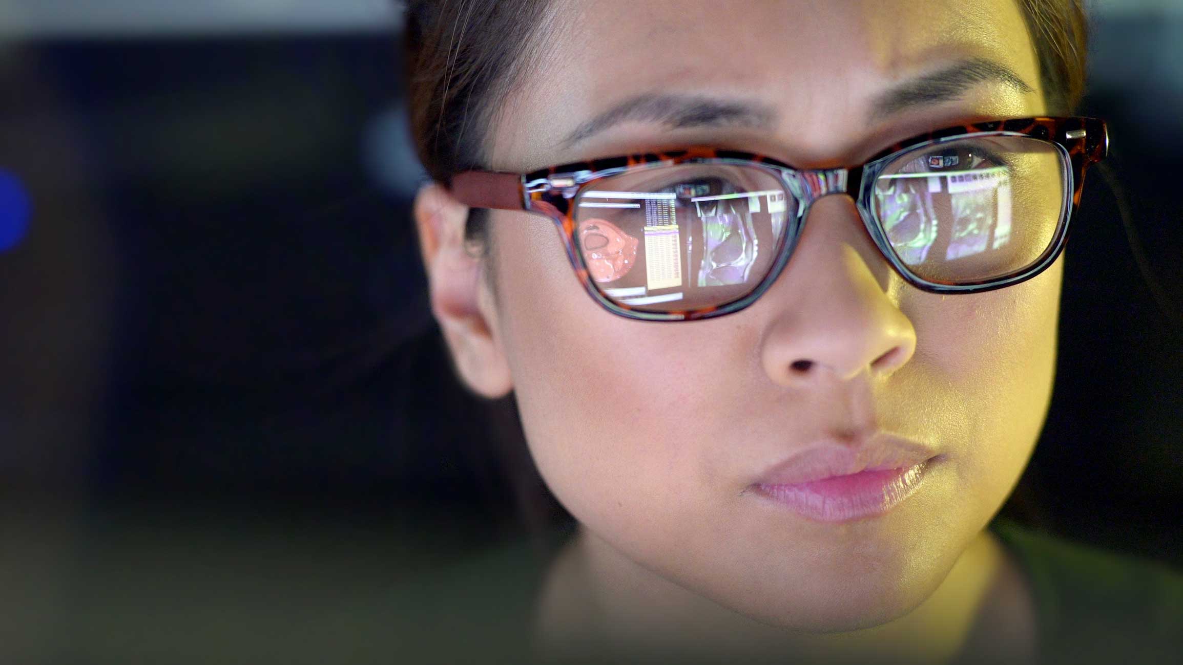 A woman wearing glasses, computer screens reflected, focused on Digital Forensics Planning.