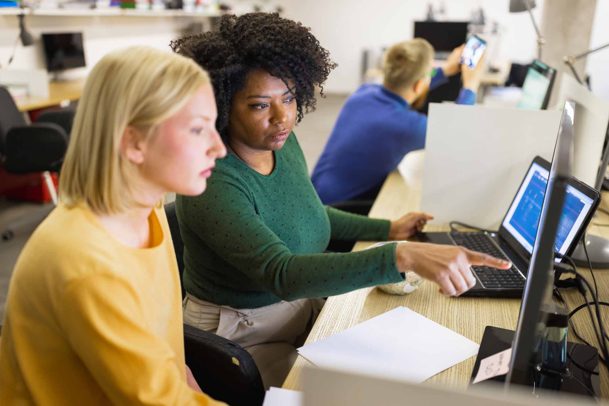 Two women discuss strategic data breach planning while working at a computer in a modern office.