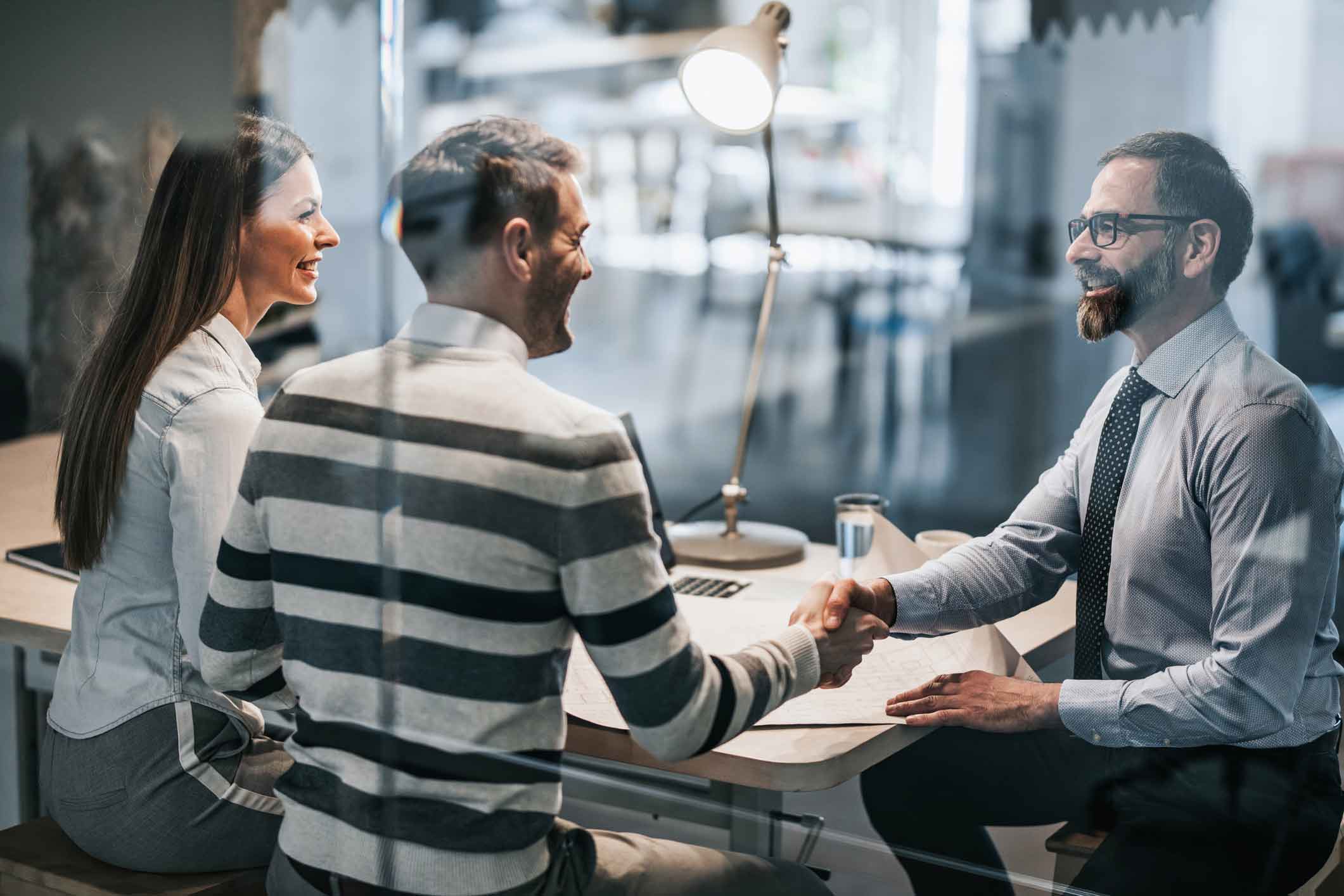 Three people in an office meeting discuss IAM Strategic Planning; two men shake hands, woman smiles.