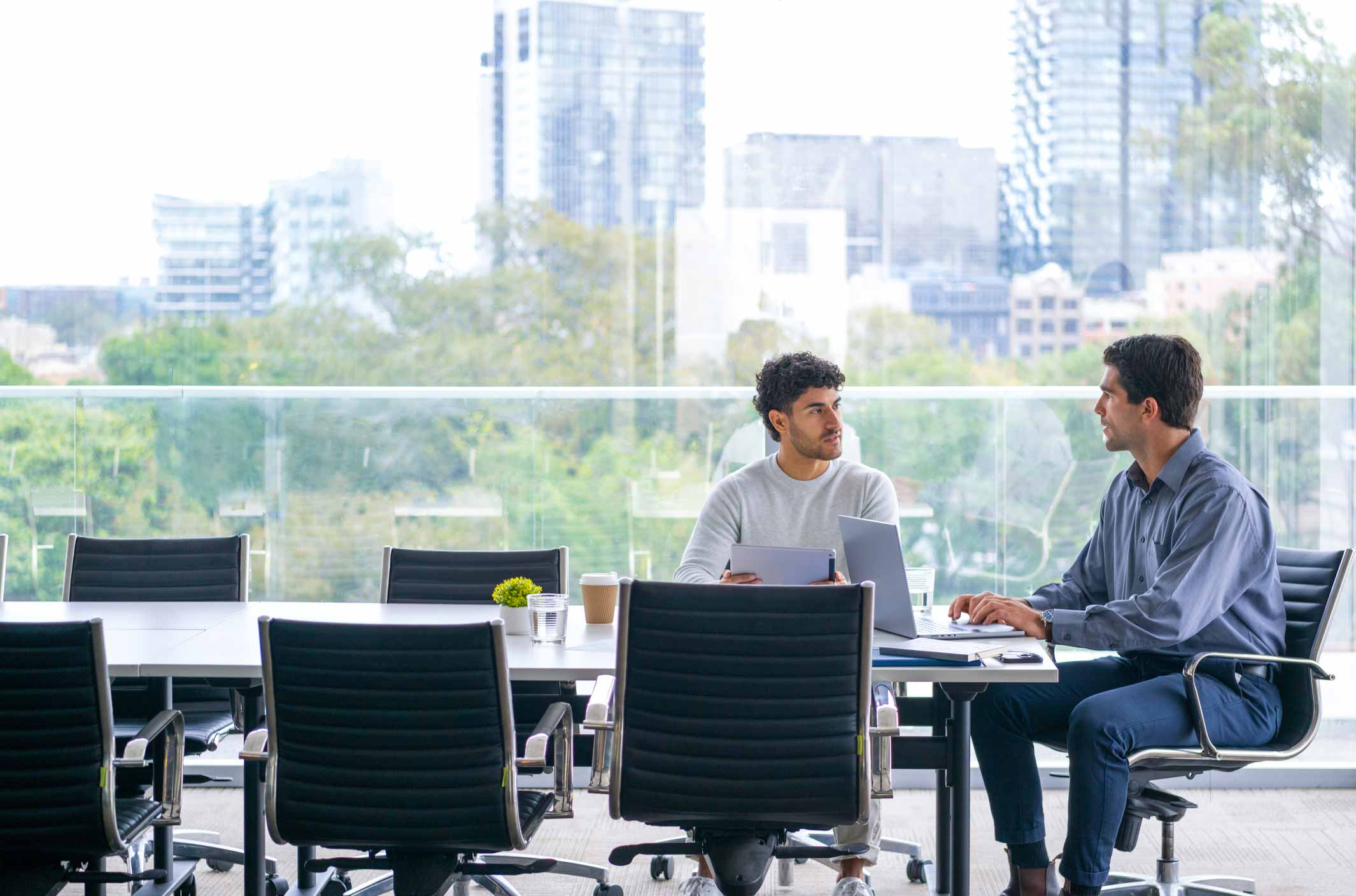 Two men discuss cybersecurity strategic planning at a conference table in a modern office.