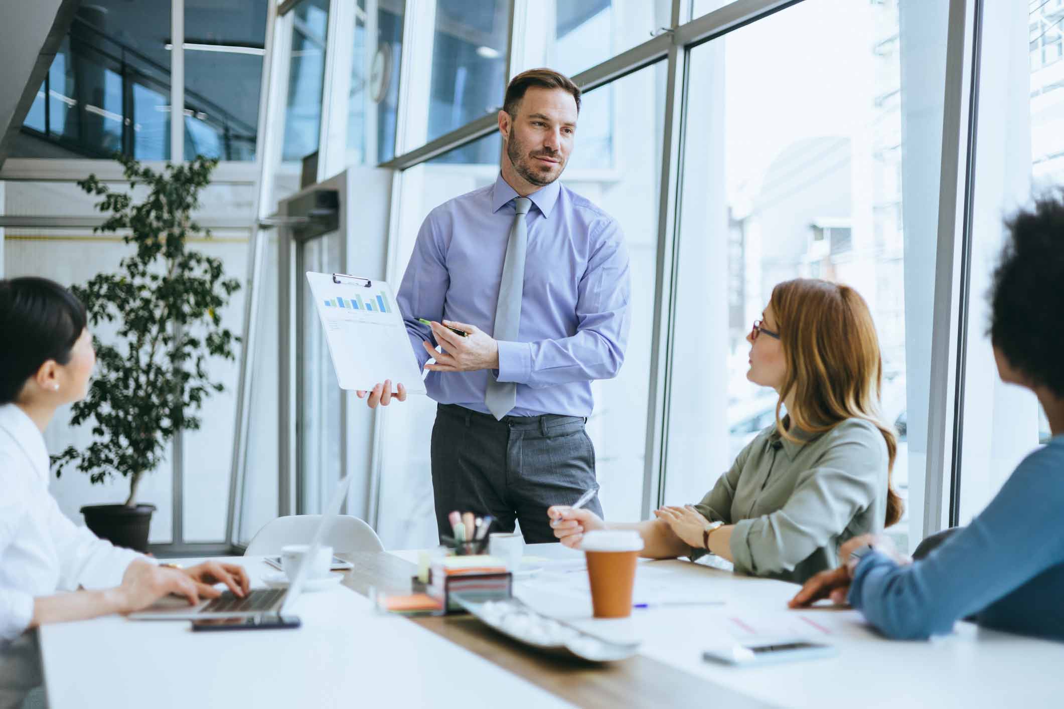 Man presenting a chart on document management to three colleagues in a modern office meeting room.