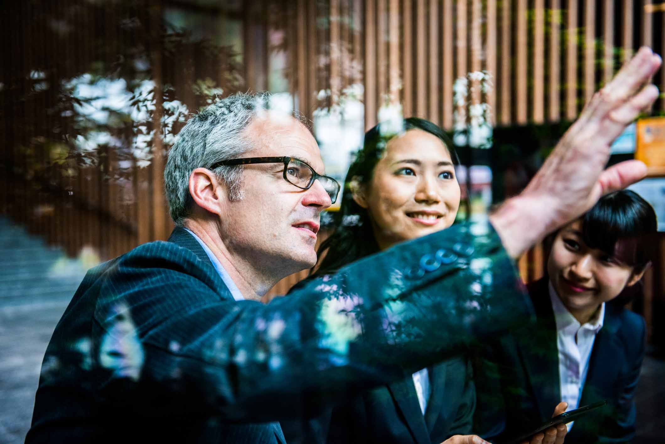 Three businesspeople in suits discuss machine learning and strategic planning by a glass window.