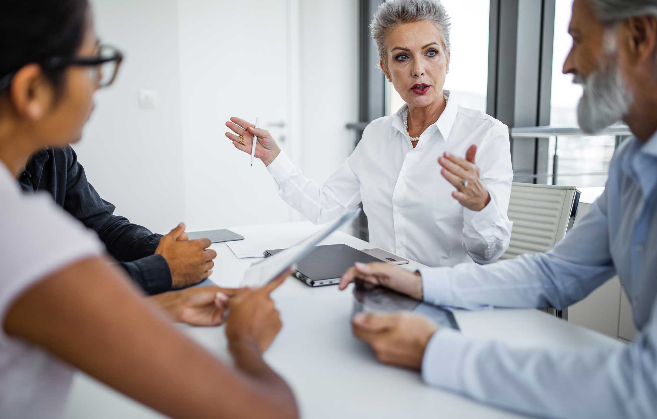 Three people in a business meeting discuss eDiscovery planning as others listen and hold tablets.