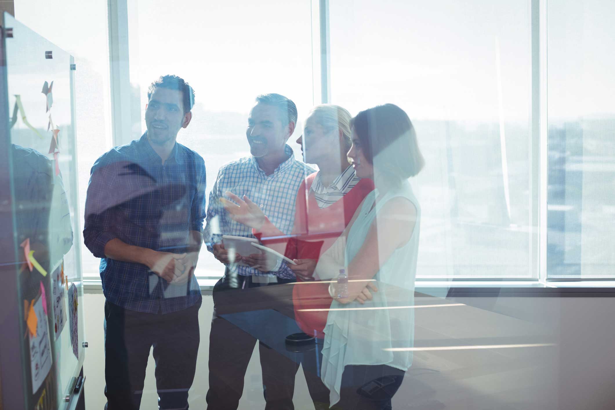 Four people discuss information security strategy by a whiteboard with sticky notes in an office.