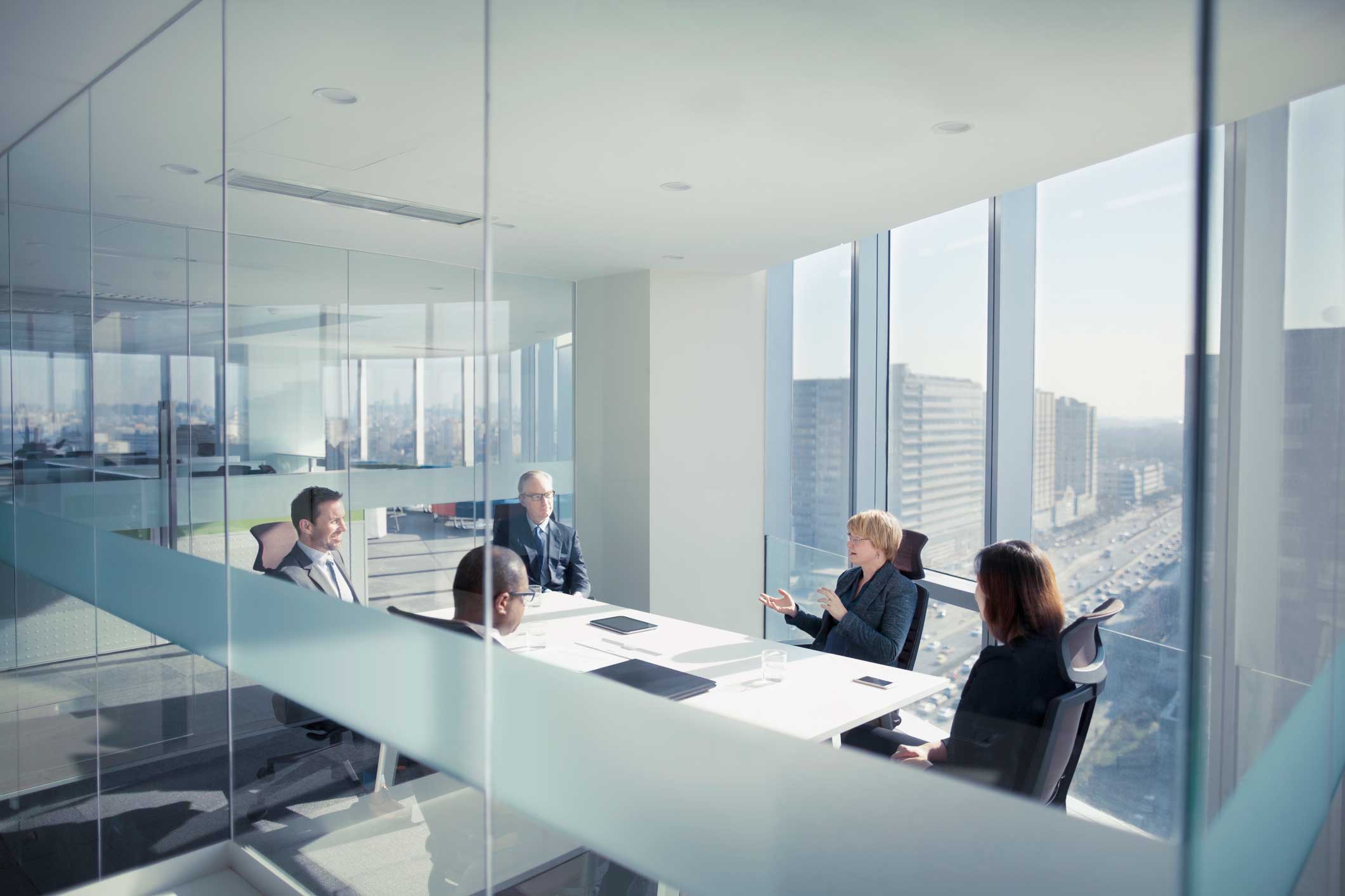 Five people in business attire discuss law firm financial management in a city-view conference room.