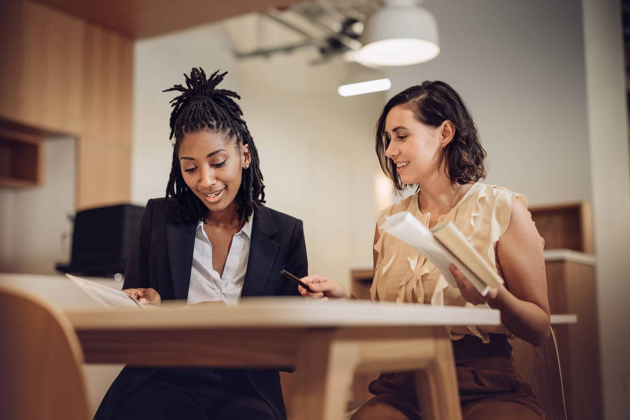 Two women smiling and reviewing documents during compensation strategy planning in an office.
