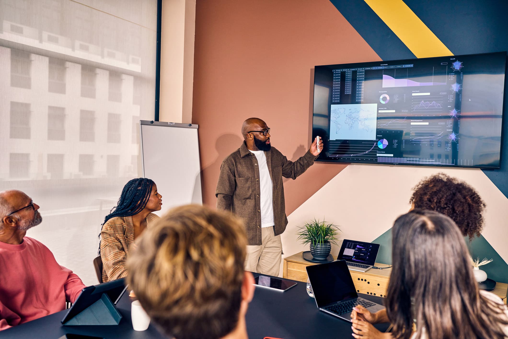 A man presents Corporate Tax Planning charts to a group in a modern office meeting room.