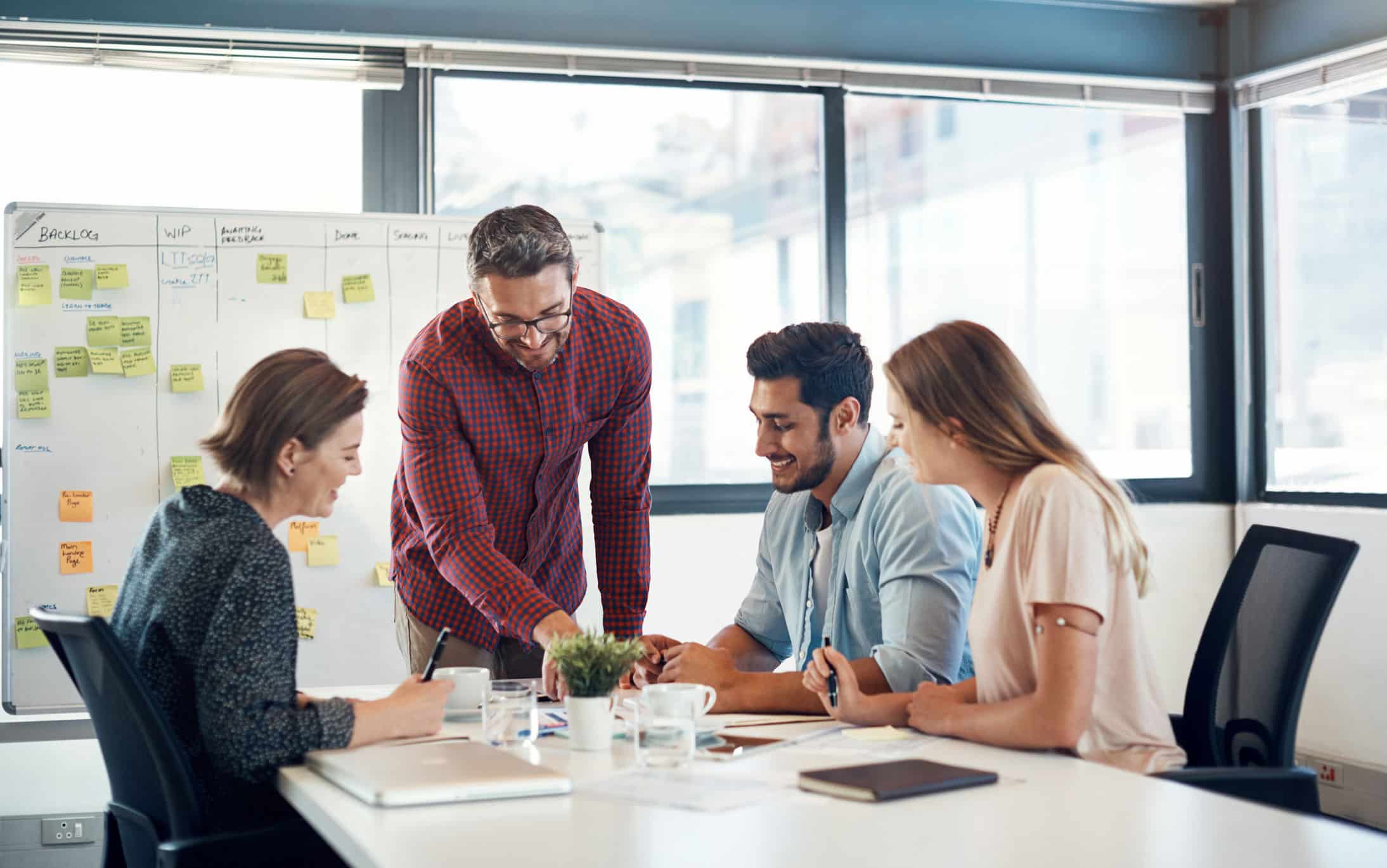 Four people discuss NLP Strategic Readiness in a modern office with a whiteboard and sticky notes.
