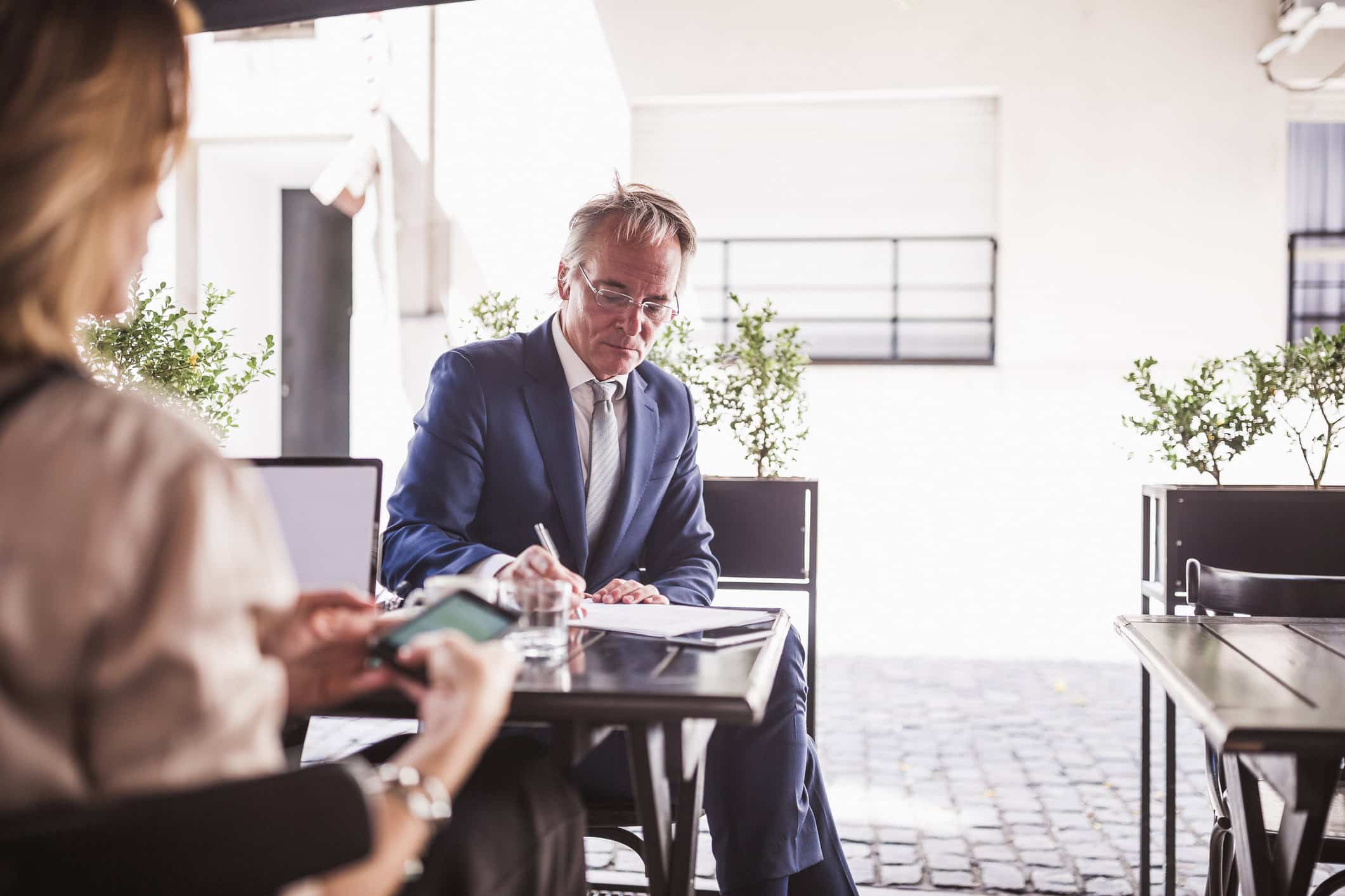 Man in suit writing outdoors, woman in foreground with phone—change management reinforcement.