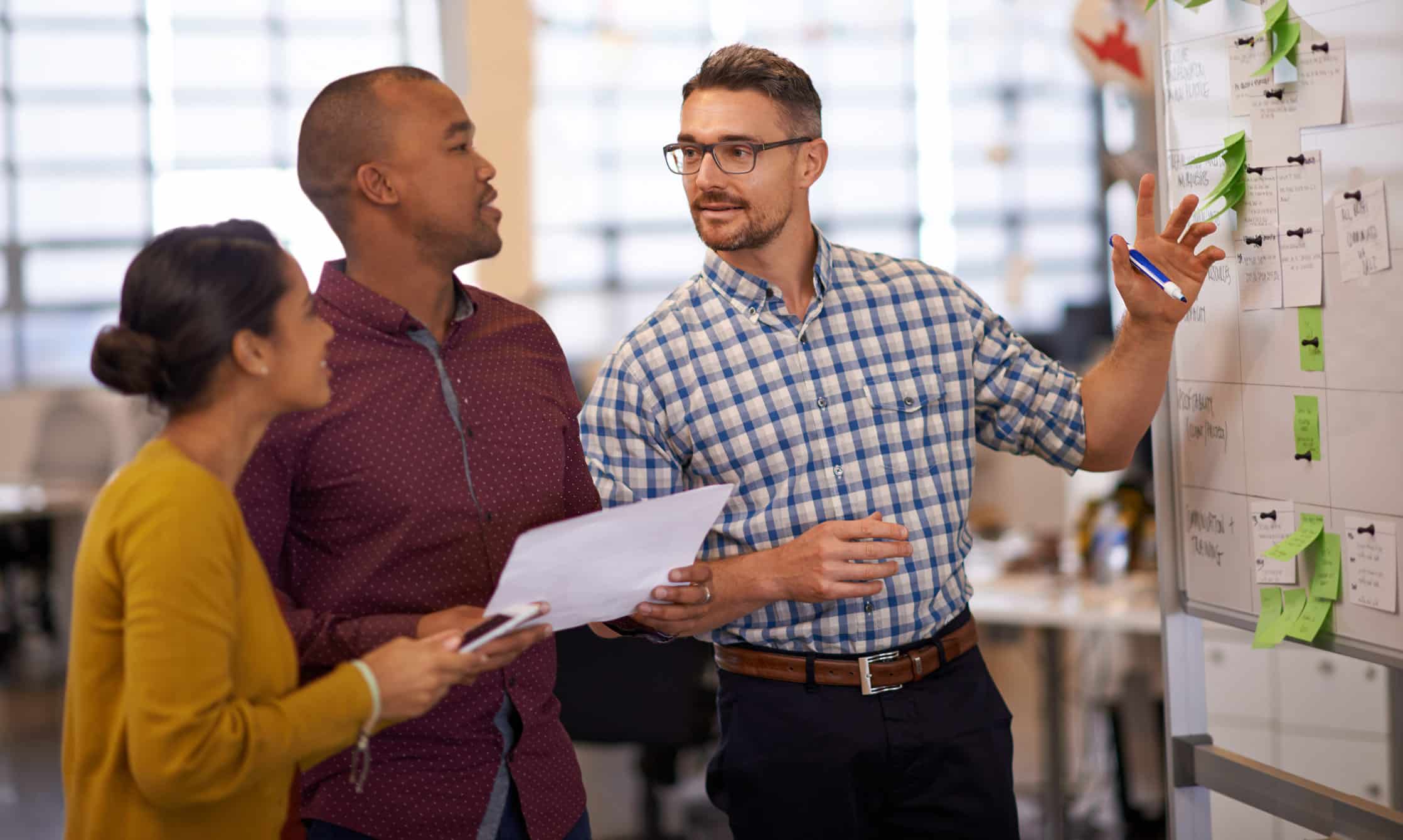 Three people discuss Modern Data Architecture and plans on a whiteboard in a modern office.