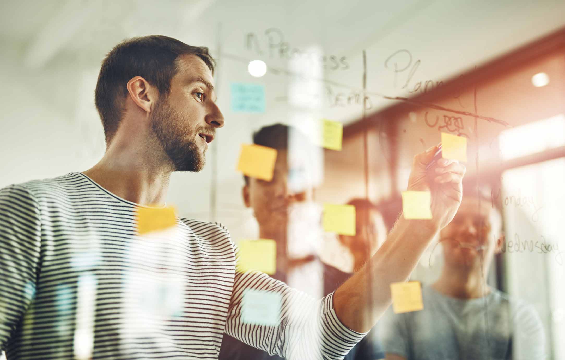 Man writing on glass board with sticky notes during a Talent & Capability Building session.
