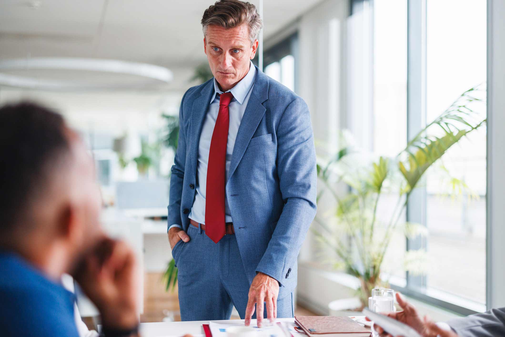 Man in blue suit at a desk, Machine Learning Consultant, looking serious during a meeting.
