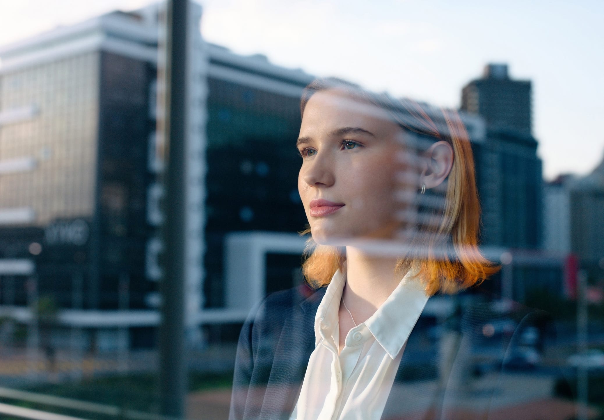 Woman in business attire gazing out, city skyline reflecting her talent & capability readiness.