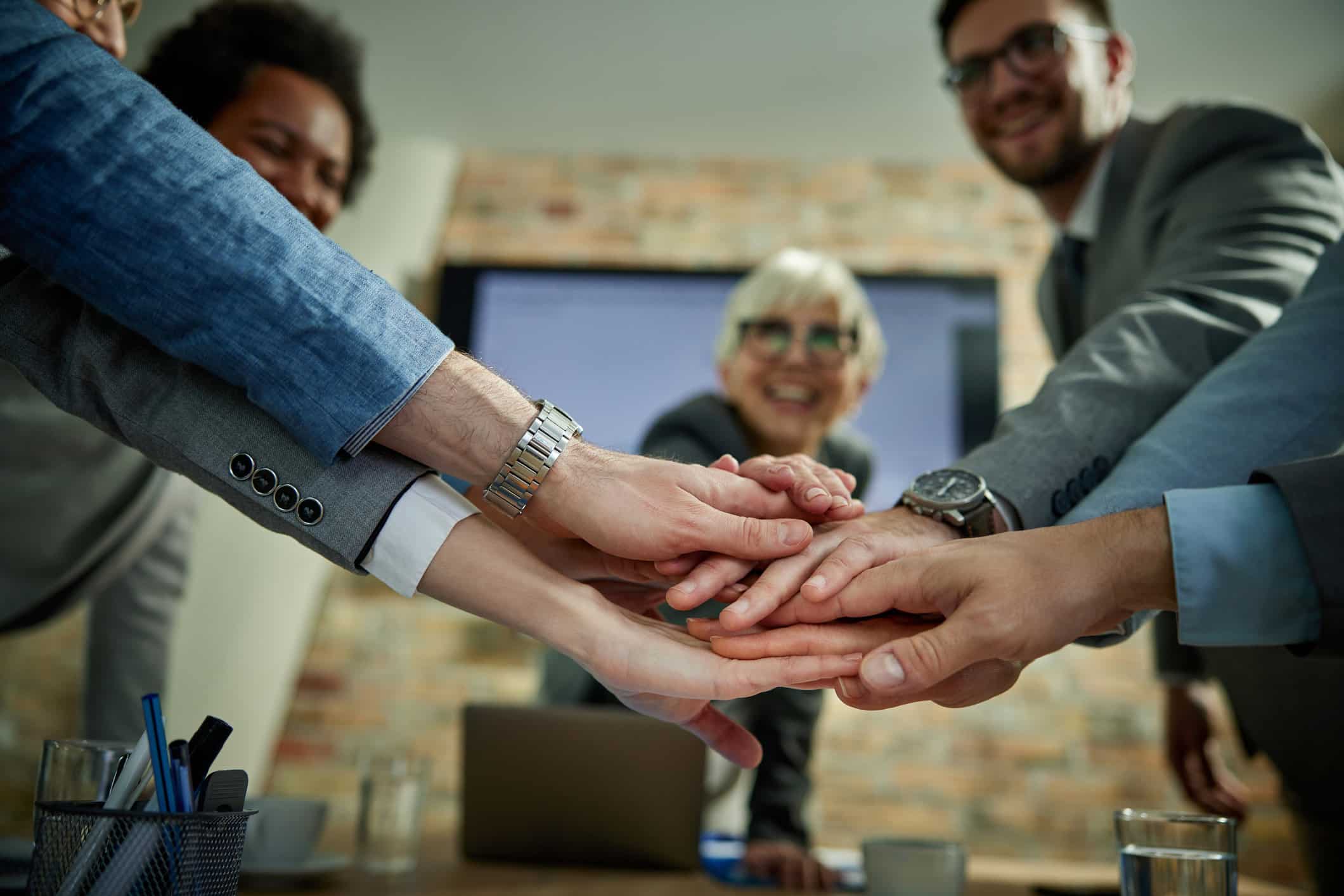 Four colleagues stack hands in a gesture of teamwork and AI Talent Enablement around a table.