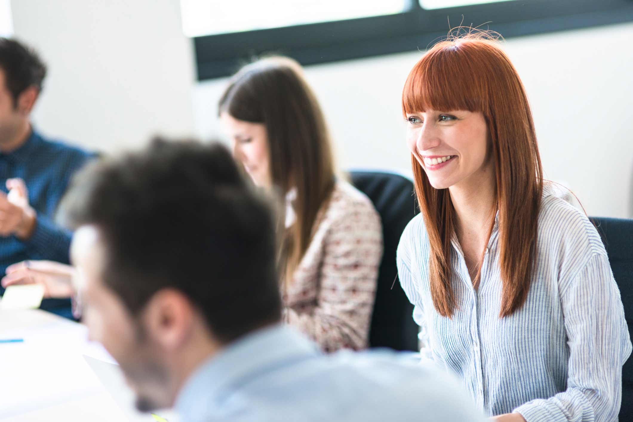 Smiling woman with red hair in a meeting discussing IAM Talent Alignment with colleagues.
