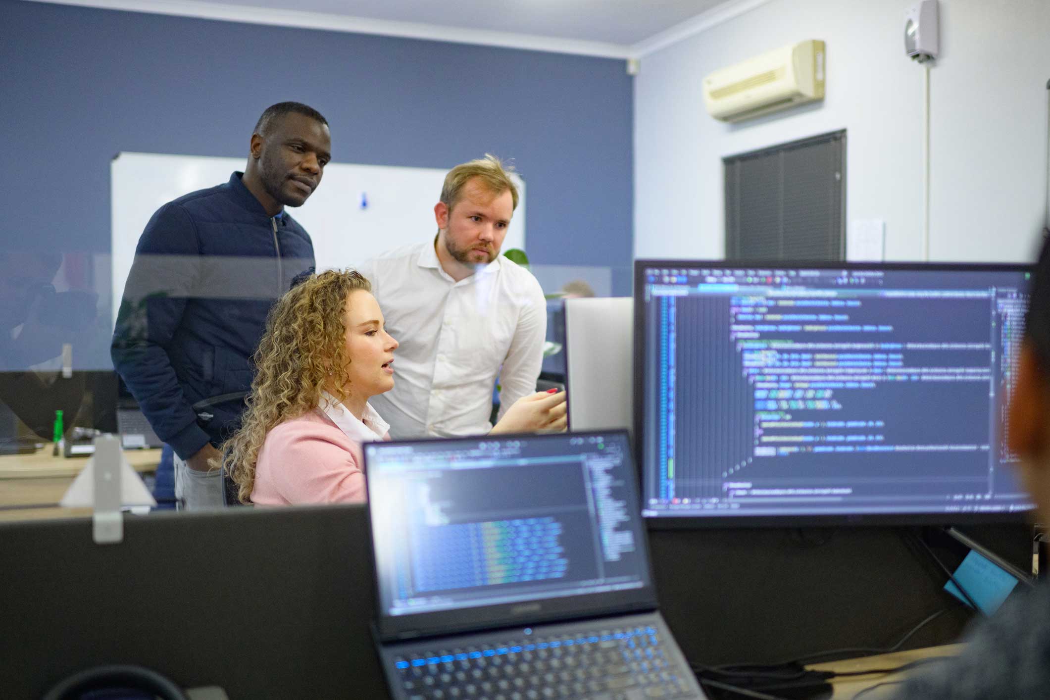 Three IT disaster recovery Talent reviewing code on computer screens in an office setting.
