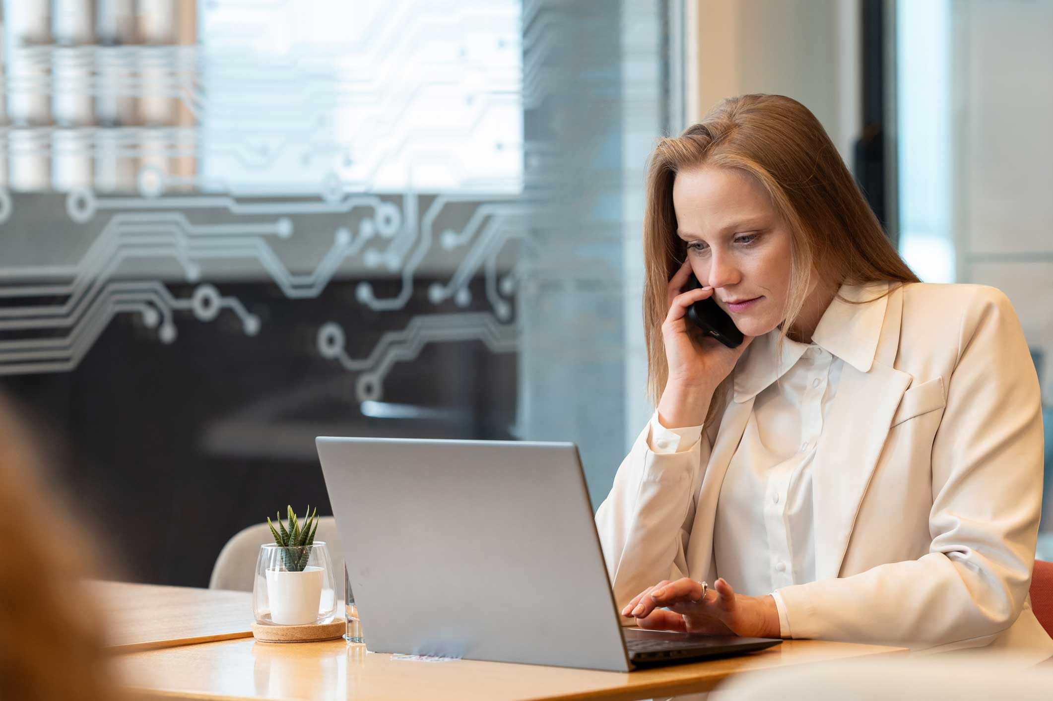 Woman in white suit discusses email security consulting while using laptop in a modern office.