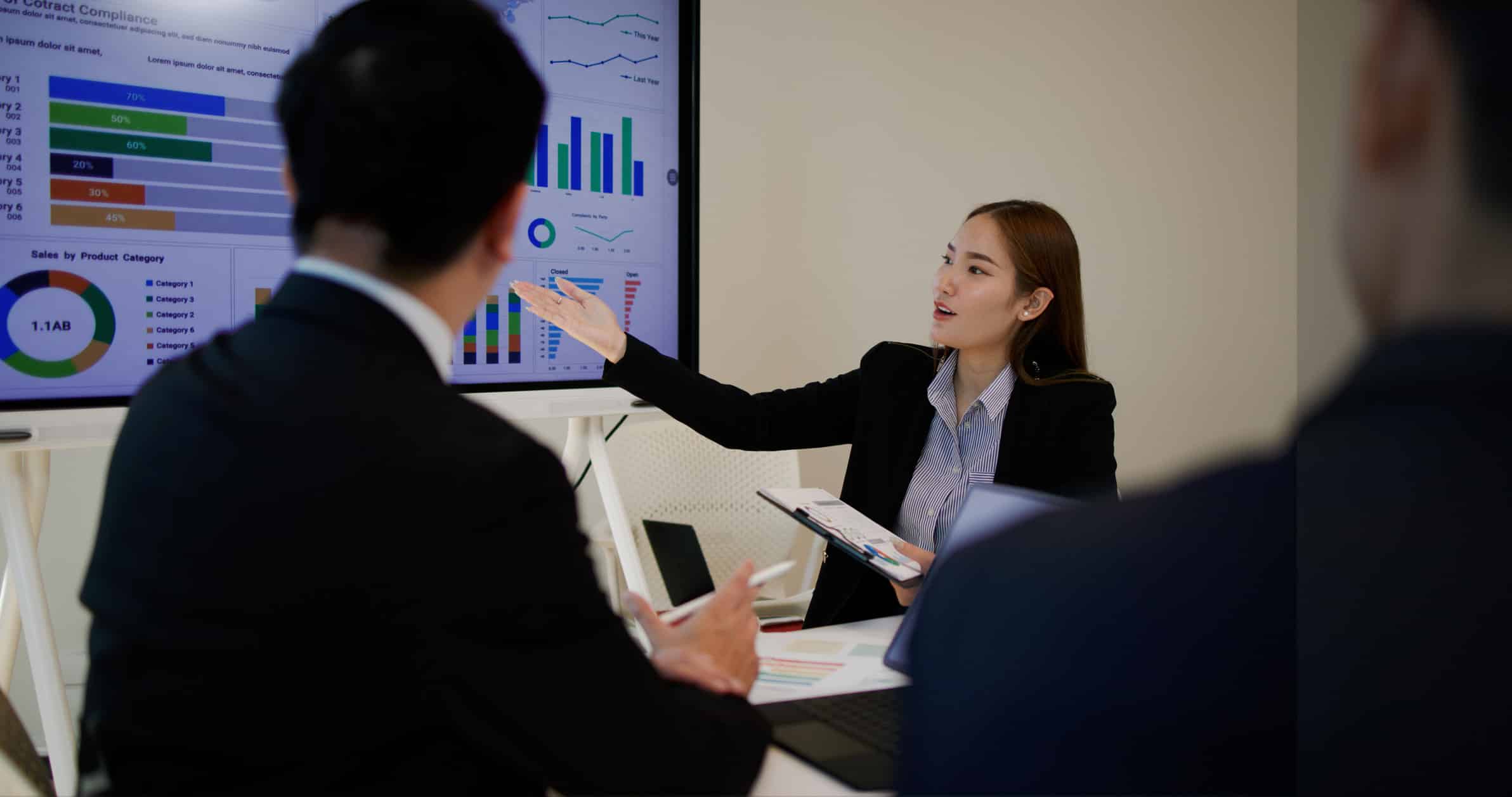 Woman presenting charts on Risk Management Technology to colleagues during a business meeting.