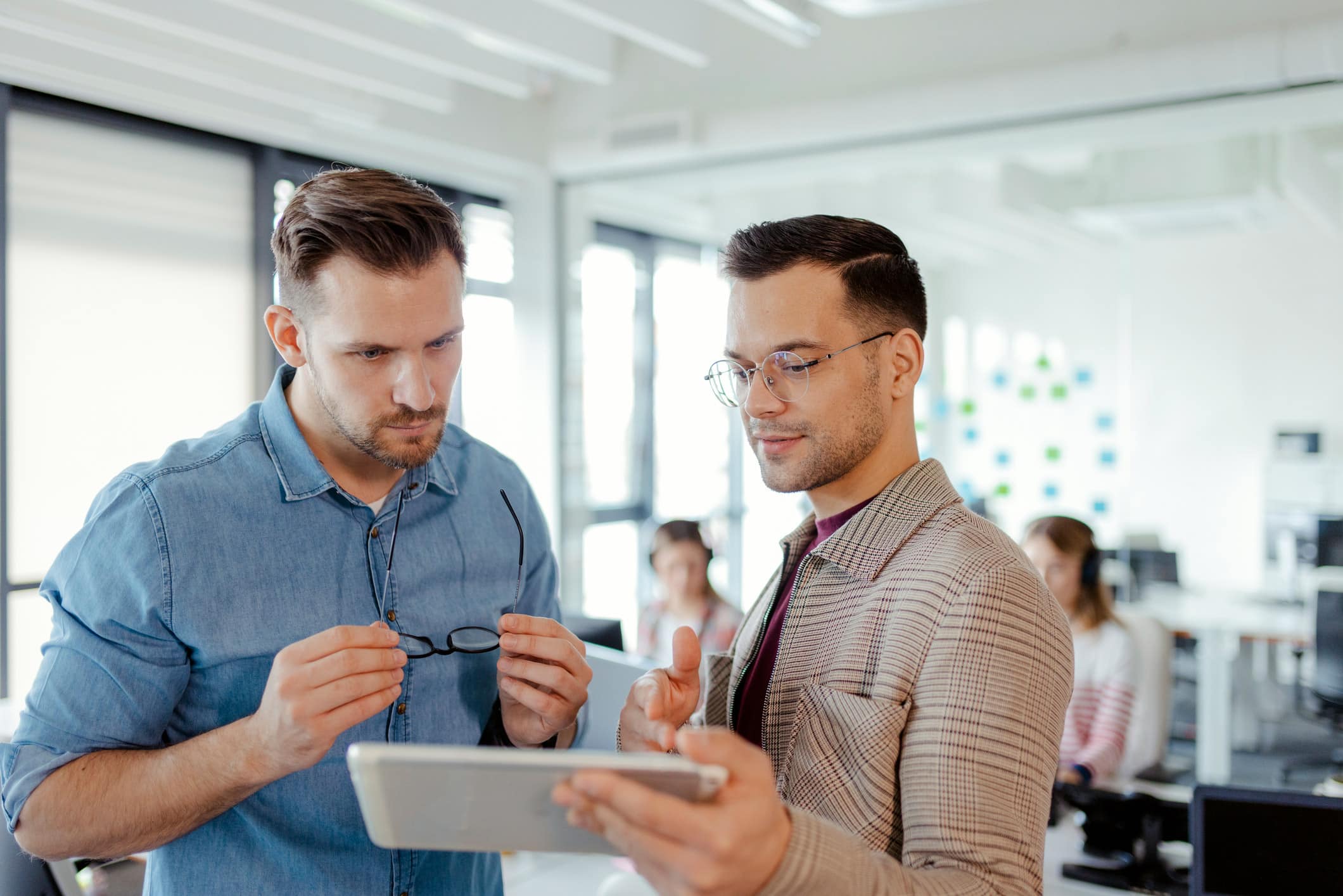Two men in an office discuss Expense Reduction Technology while looking at a tablet.
