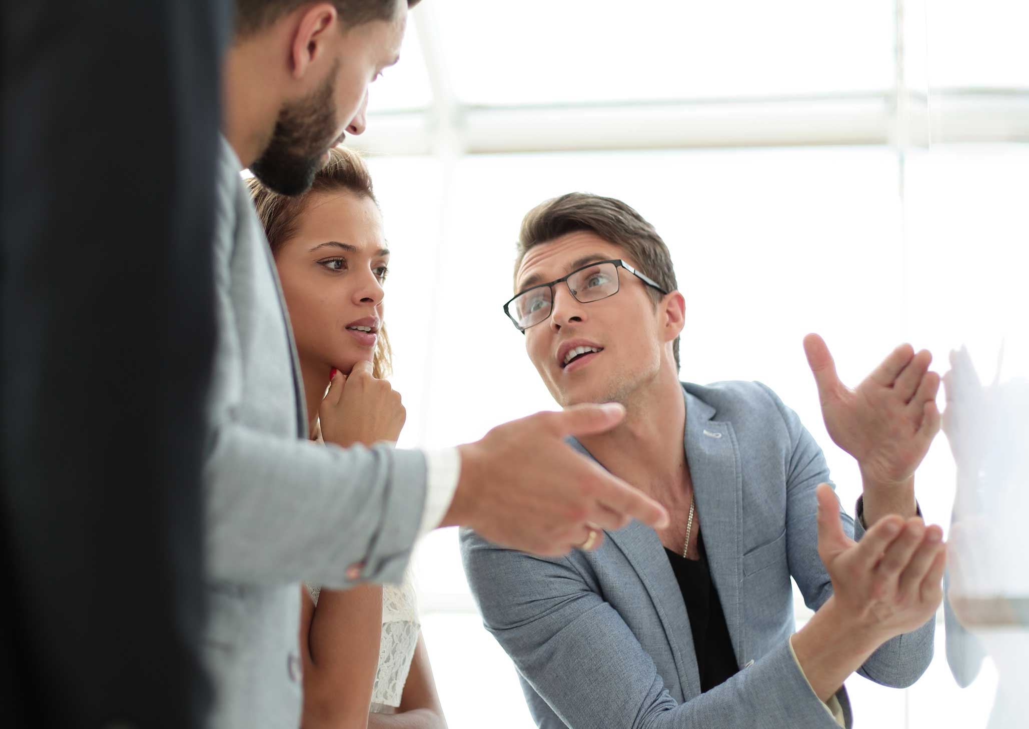 Three people in business attire discuss Law Firm Expense Management Enablement in a bright office.
