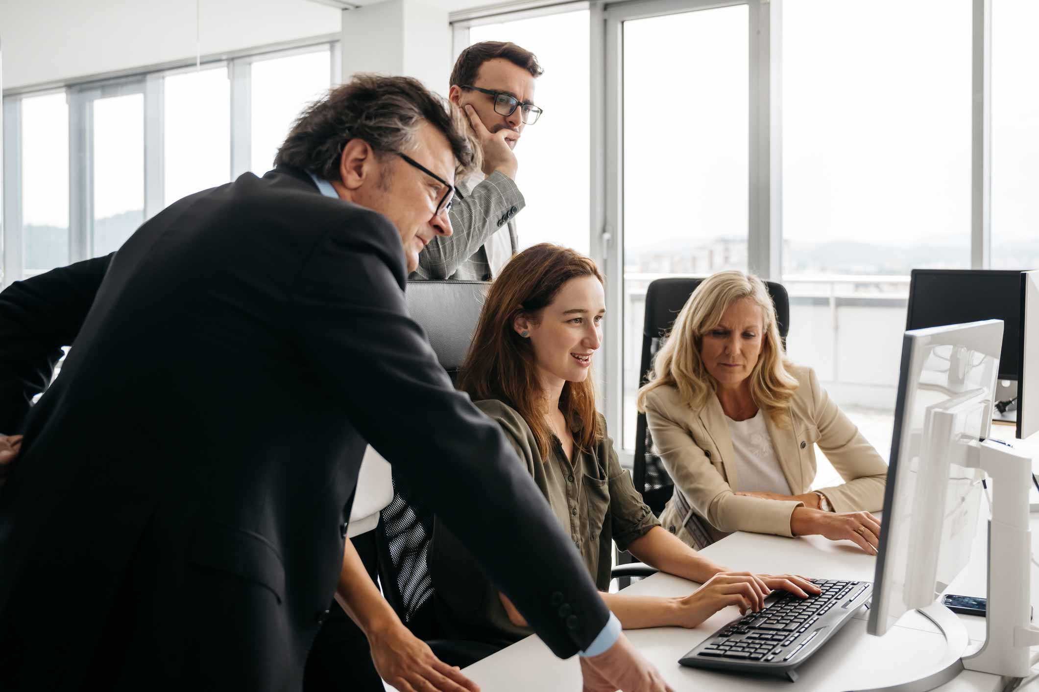 Four professionals discuss cybersecurity enablement around a computer in a bright office setting.