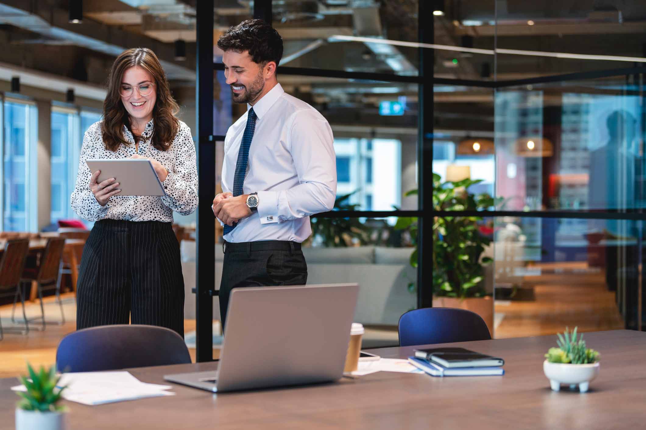 Two colleagues smiling, viewing a tablet for Document Management Enablement in a modern office.