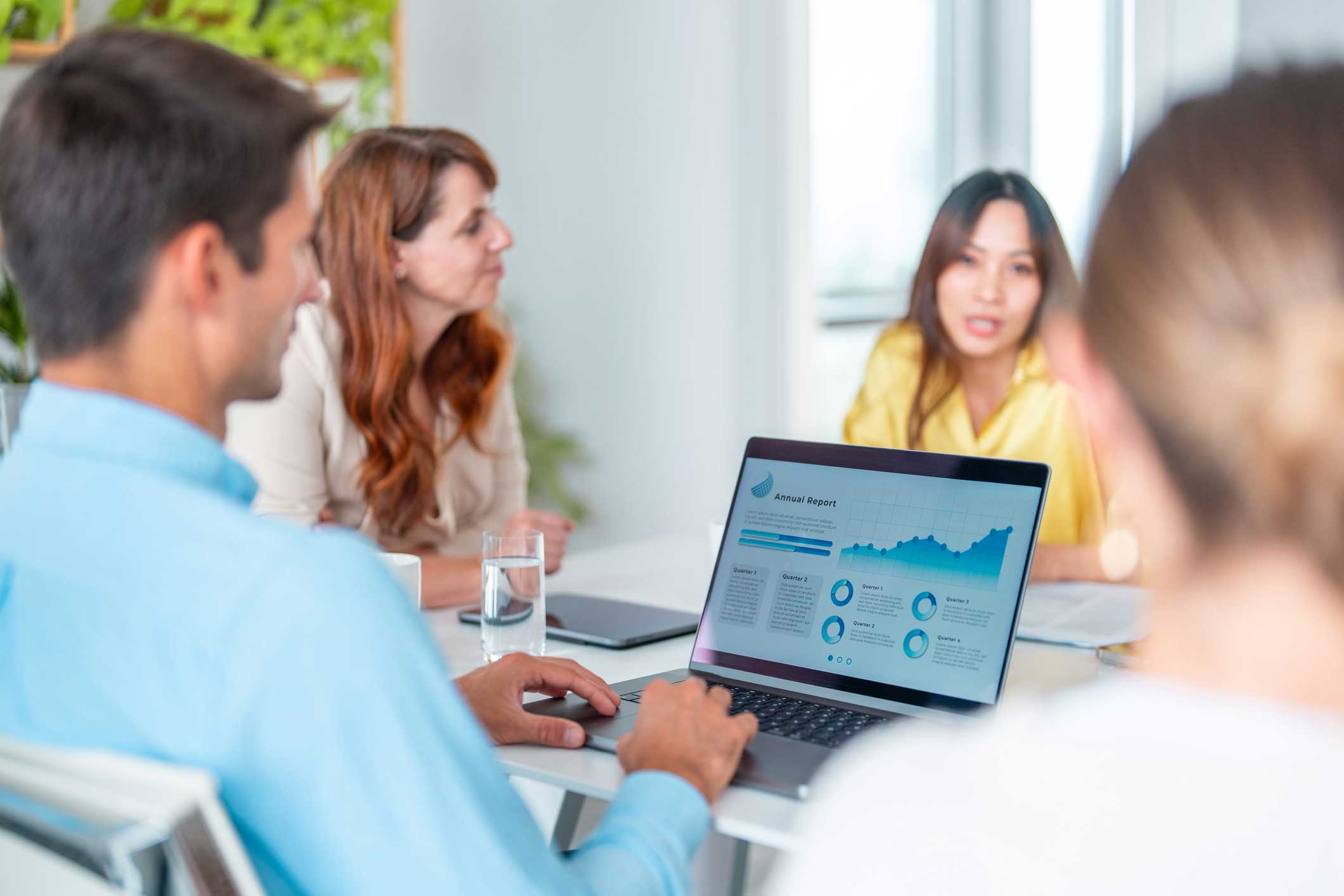 Four people meet; a laptop displays a report on Machine Learning Enablement and a graph.